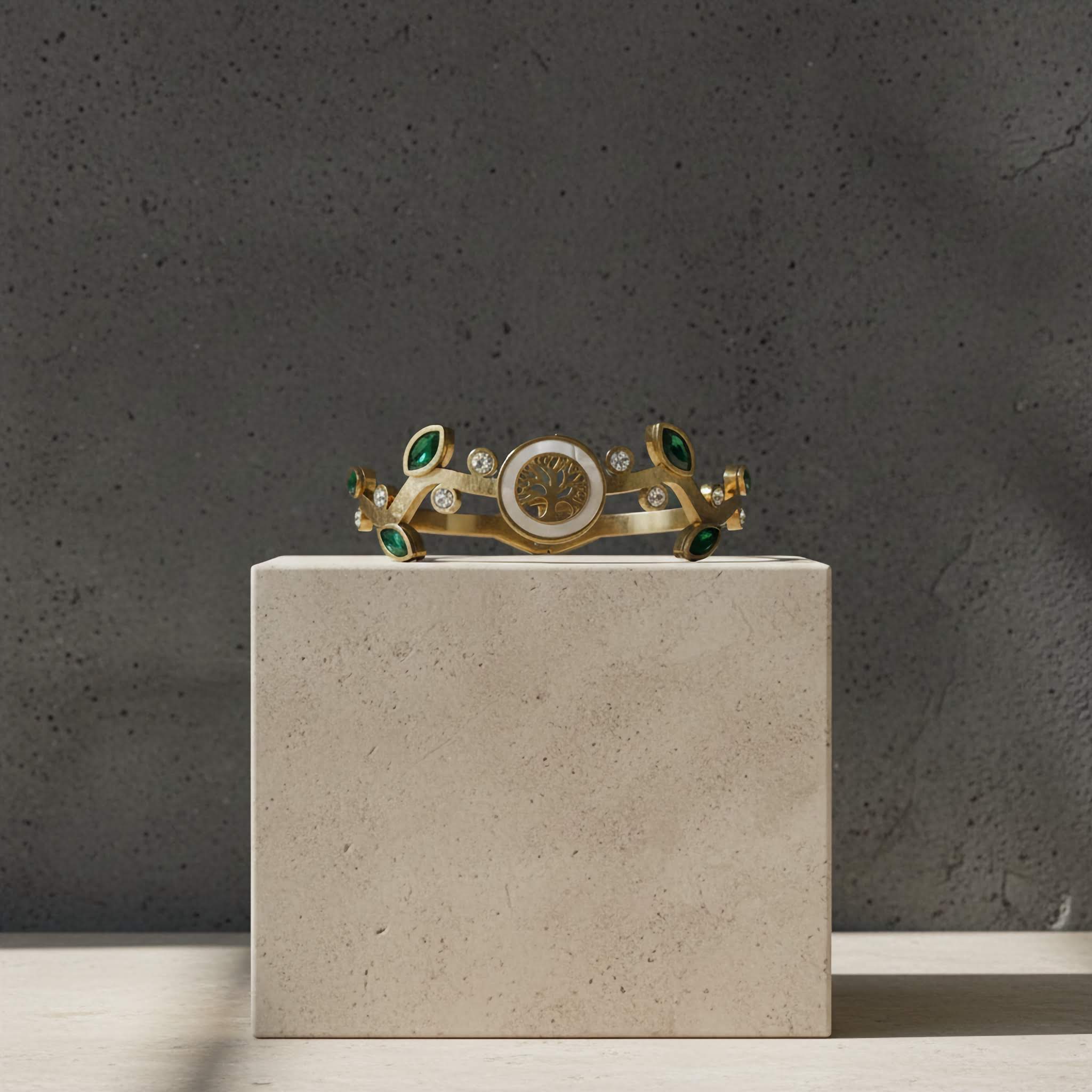 Gold tiara bracelet with green gemstones on a gray pedestal against a dark gray background