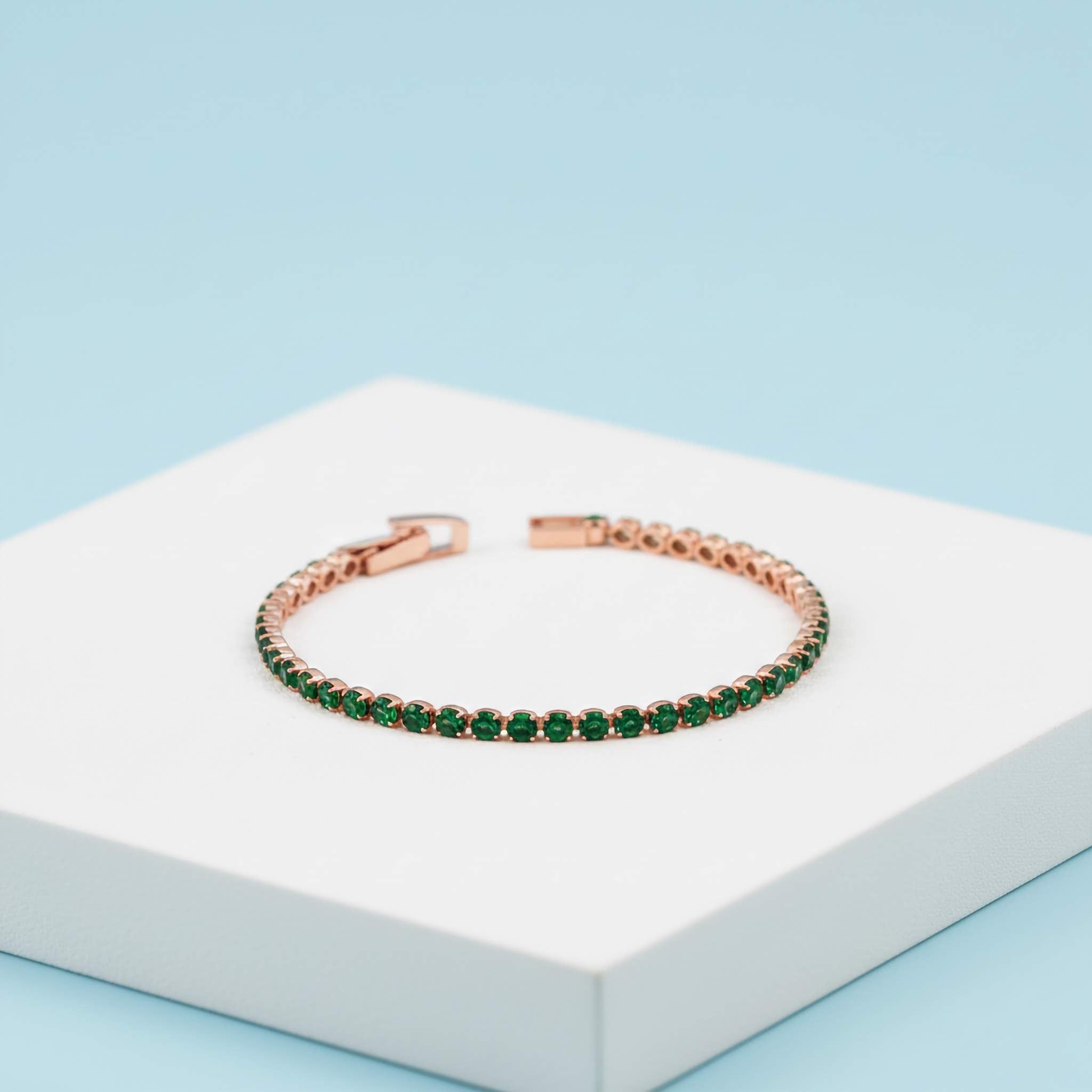 Rose gold bracelet with green gemstones on a white box with a light blue background
