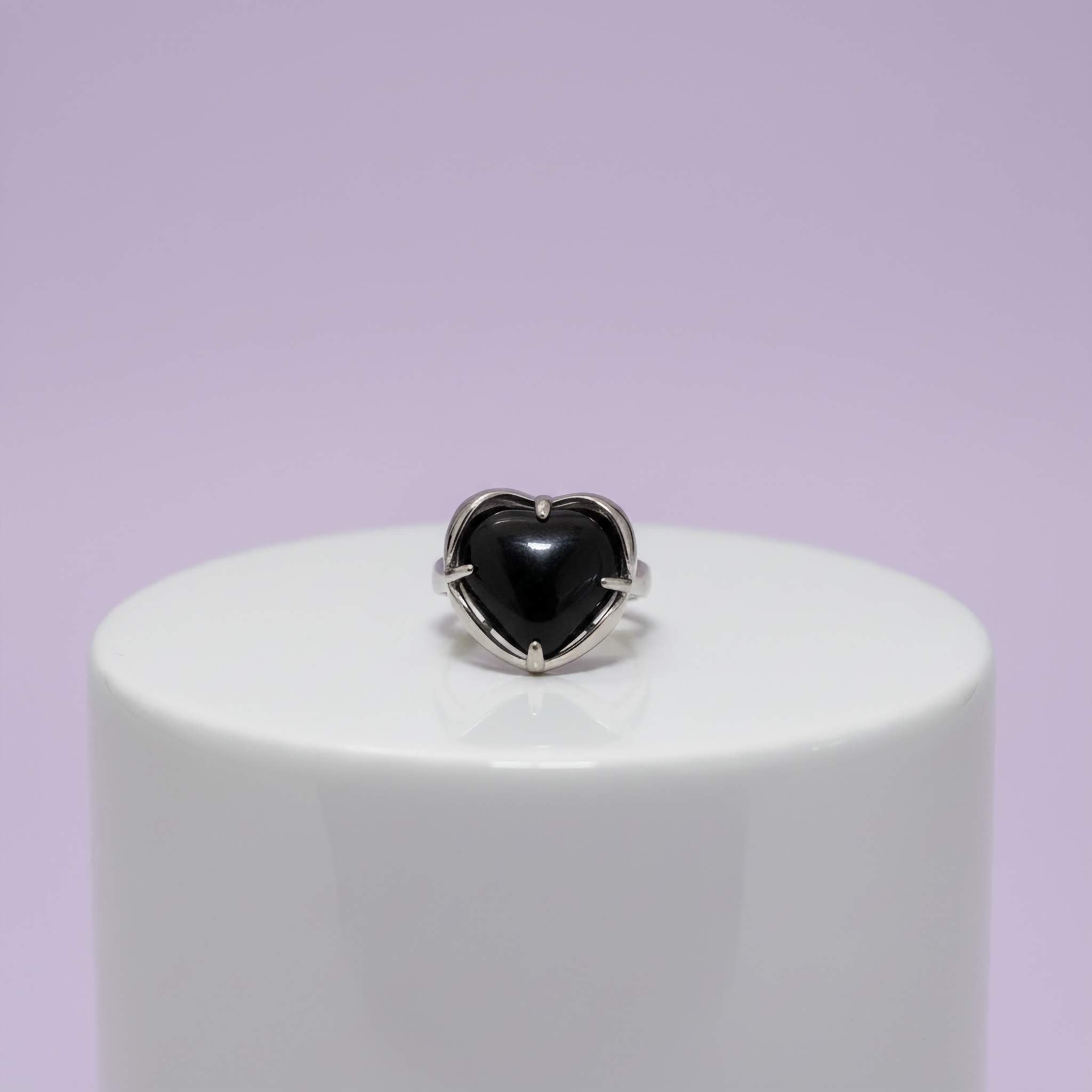 Heart-shaped black stone ring on a white stand with a light purple background
