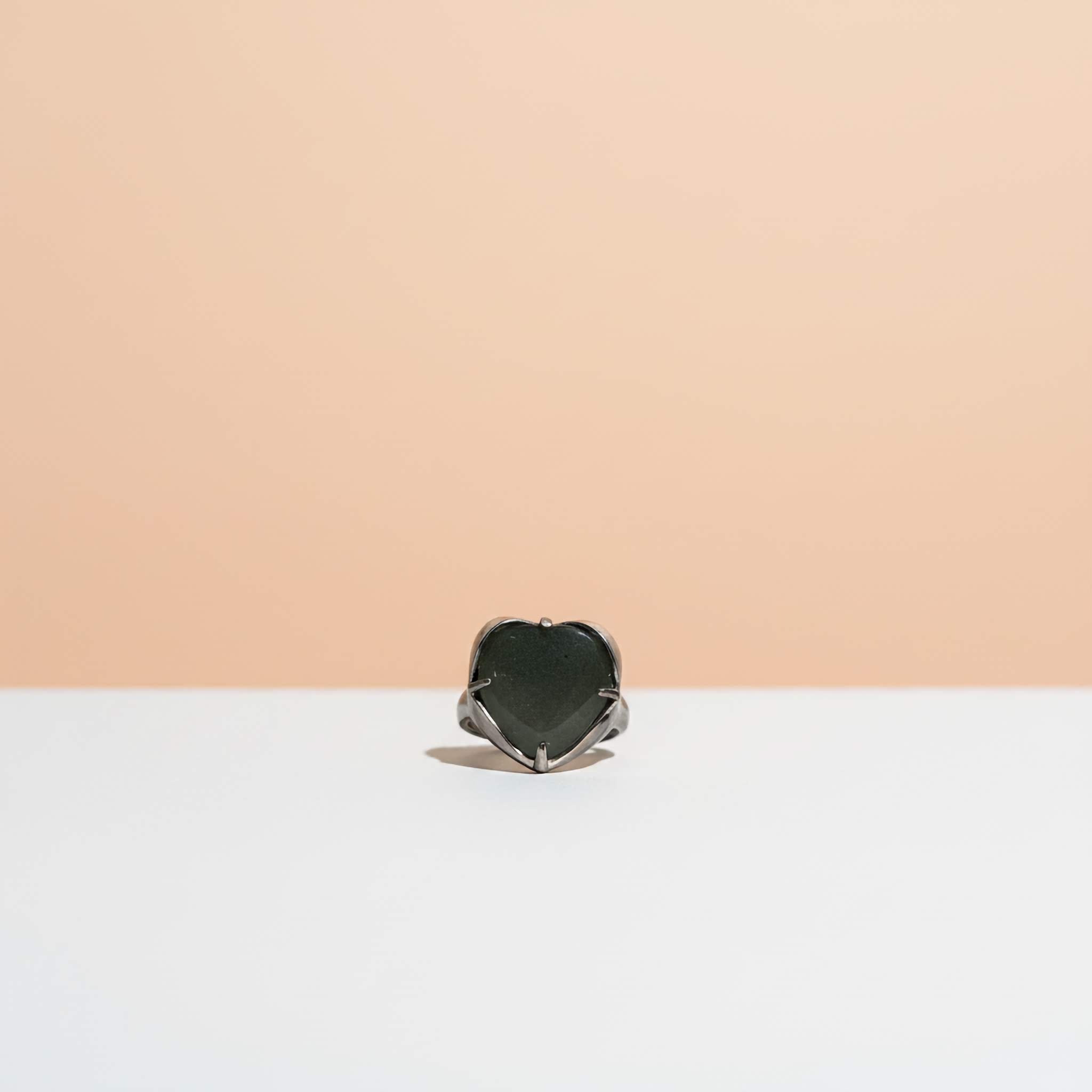 Heart-shaped dark green stone ring on a white surface with a beige background