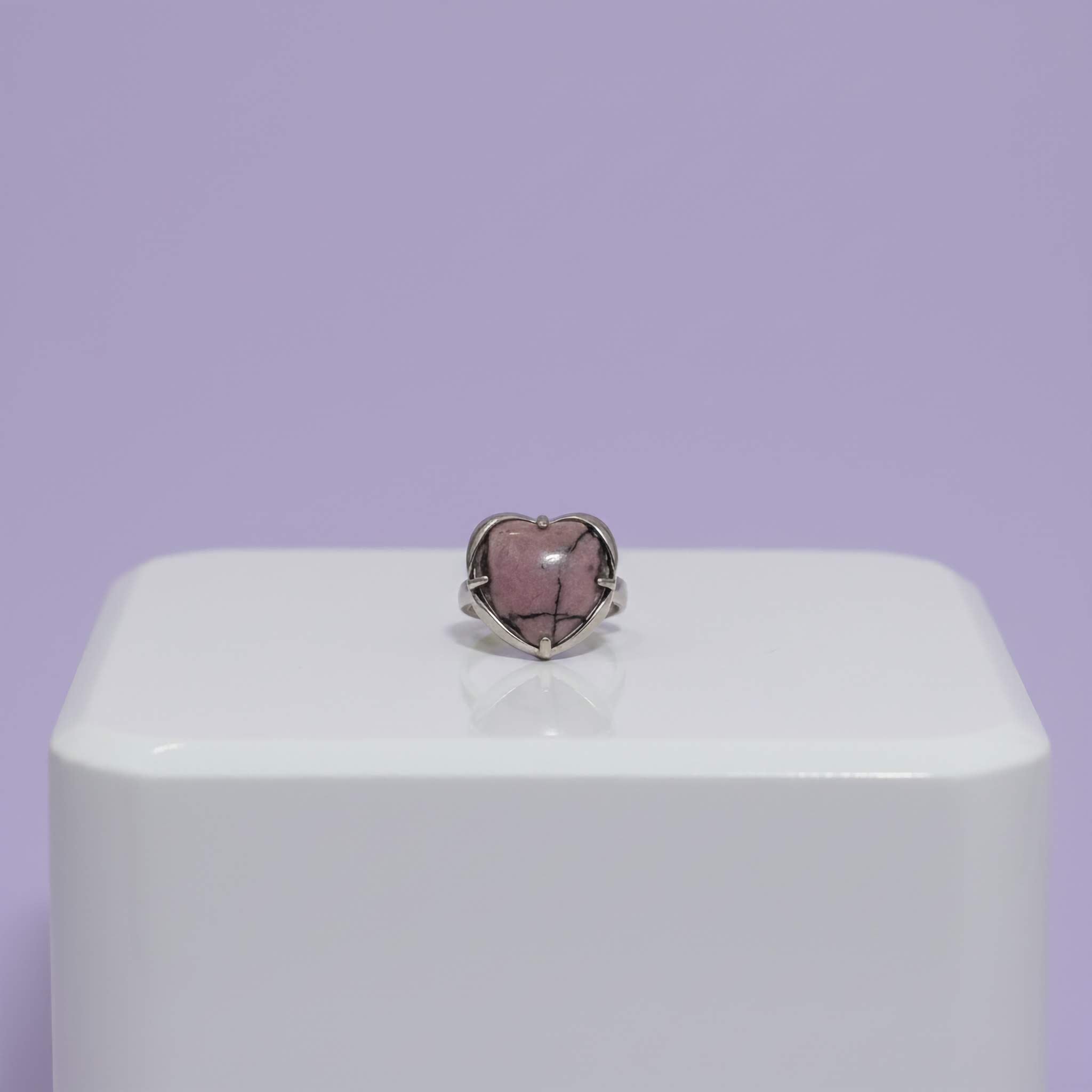 Heart-shaped purple with black accents stone ring on a white stand with a purple background