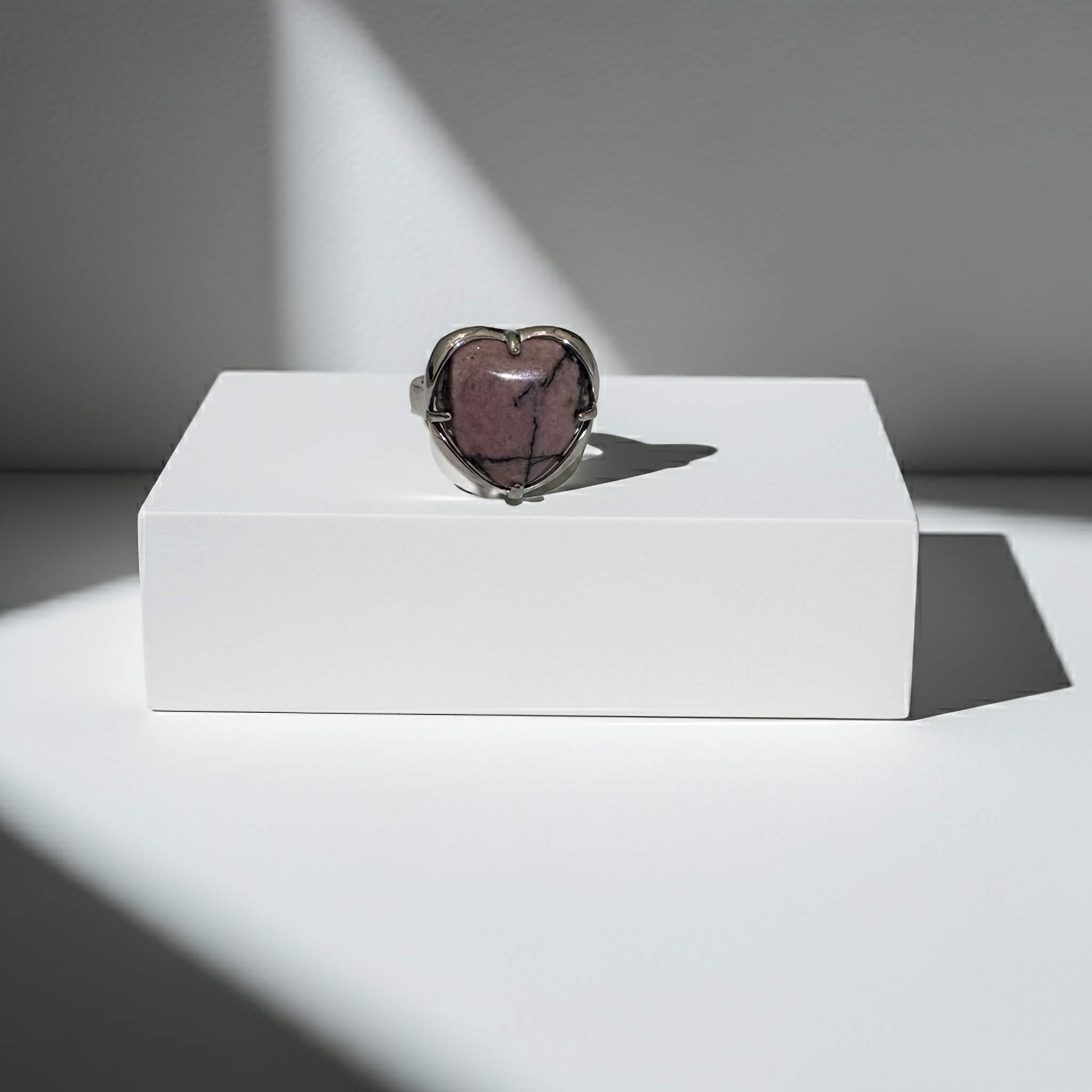 Heart-shaped ring with a purple stone on a white pedestal against a gray background