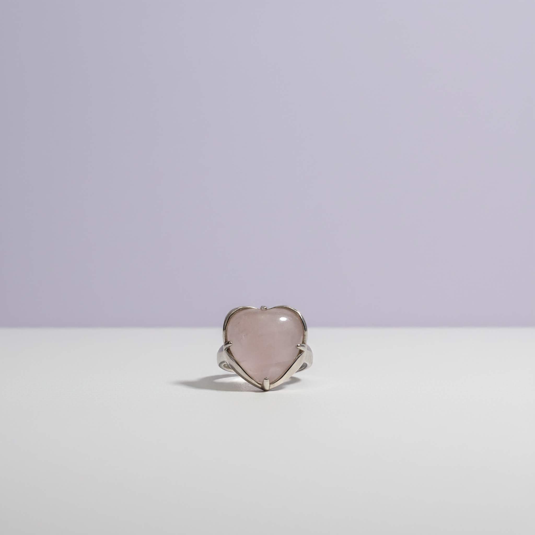 Heart-shaped ring with light pink stone on a white surface with a light purple background