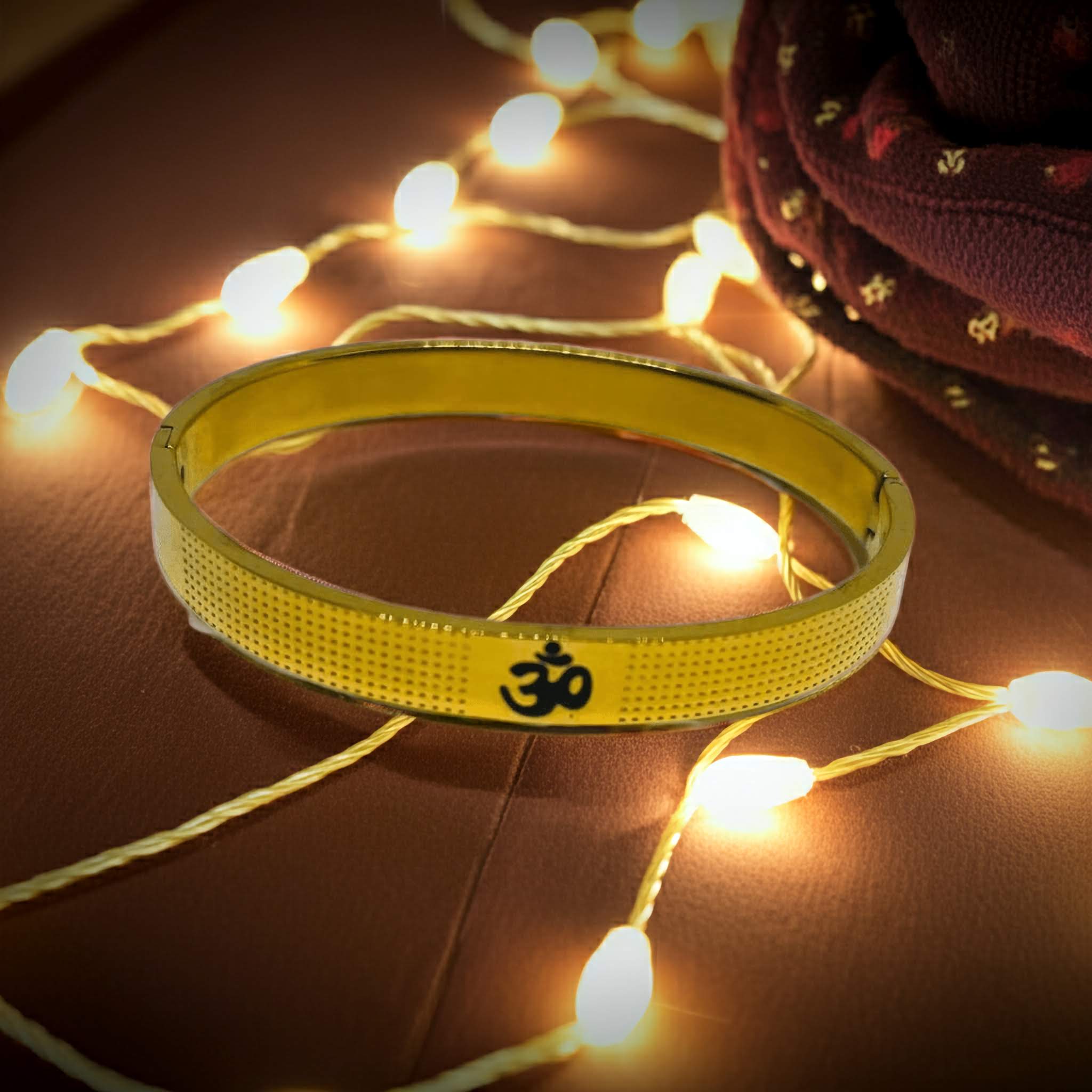 Gold bracelet with Om symbol on a wooden surface with string lights.