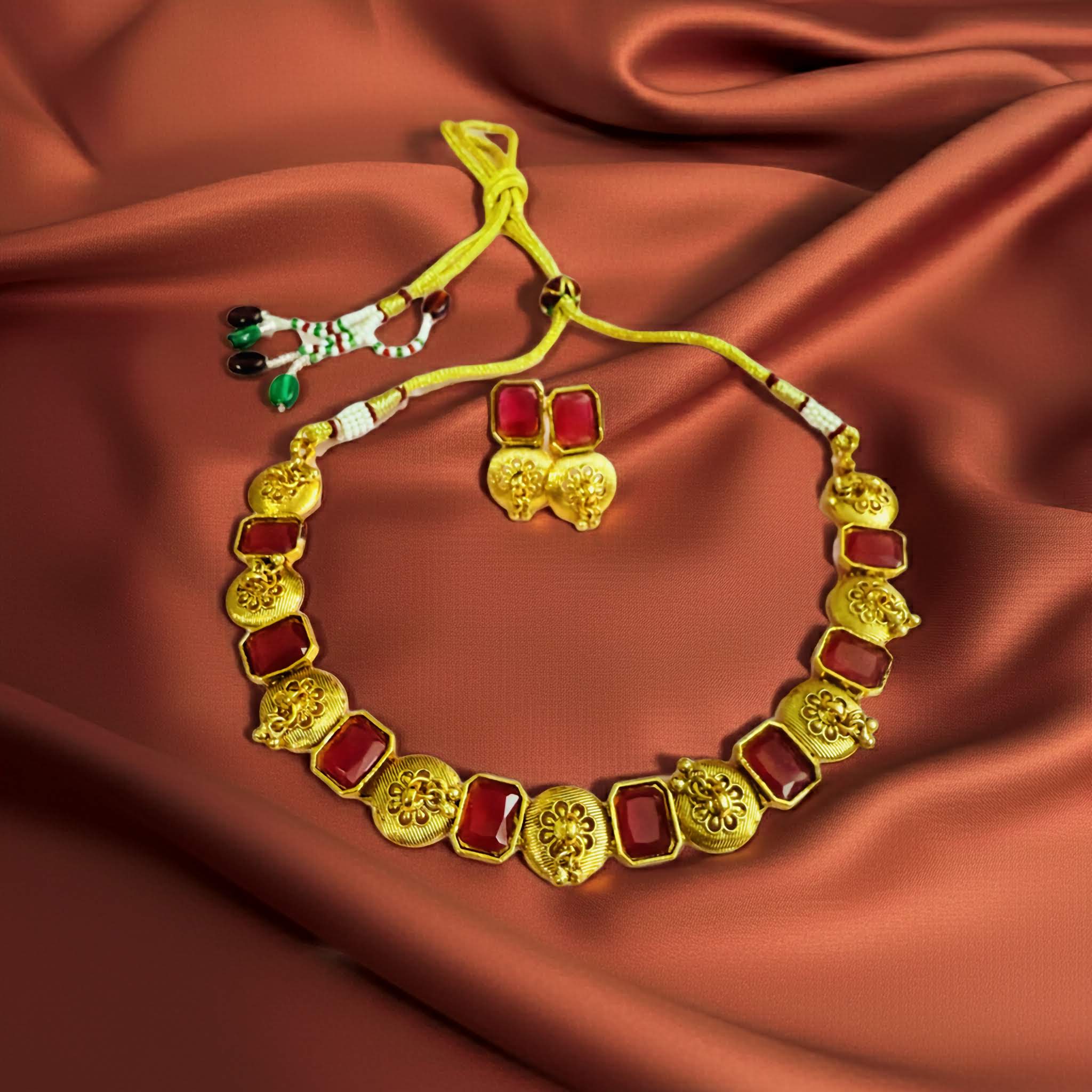 Gold necklace with red stones and matching earrings on a brown fabric background