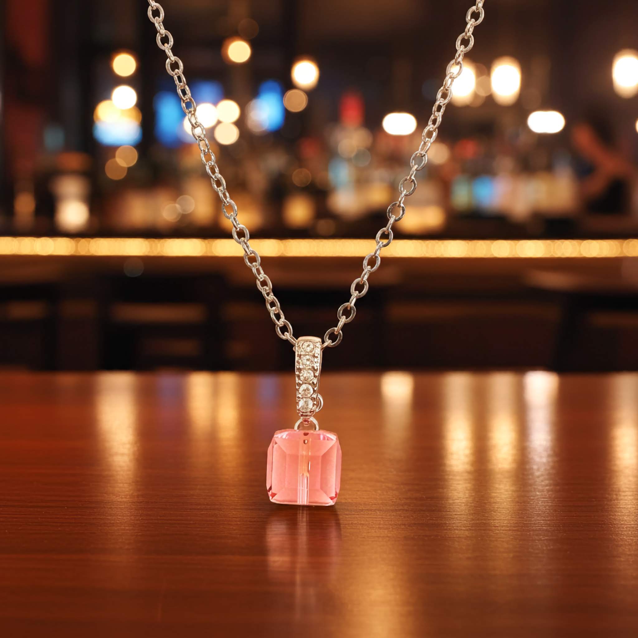 Necklace with a pink radiant cut pendant on a wooden surface with a blurred bar background