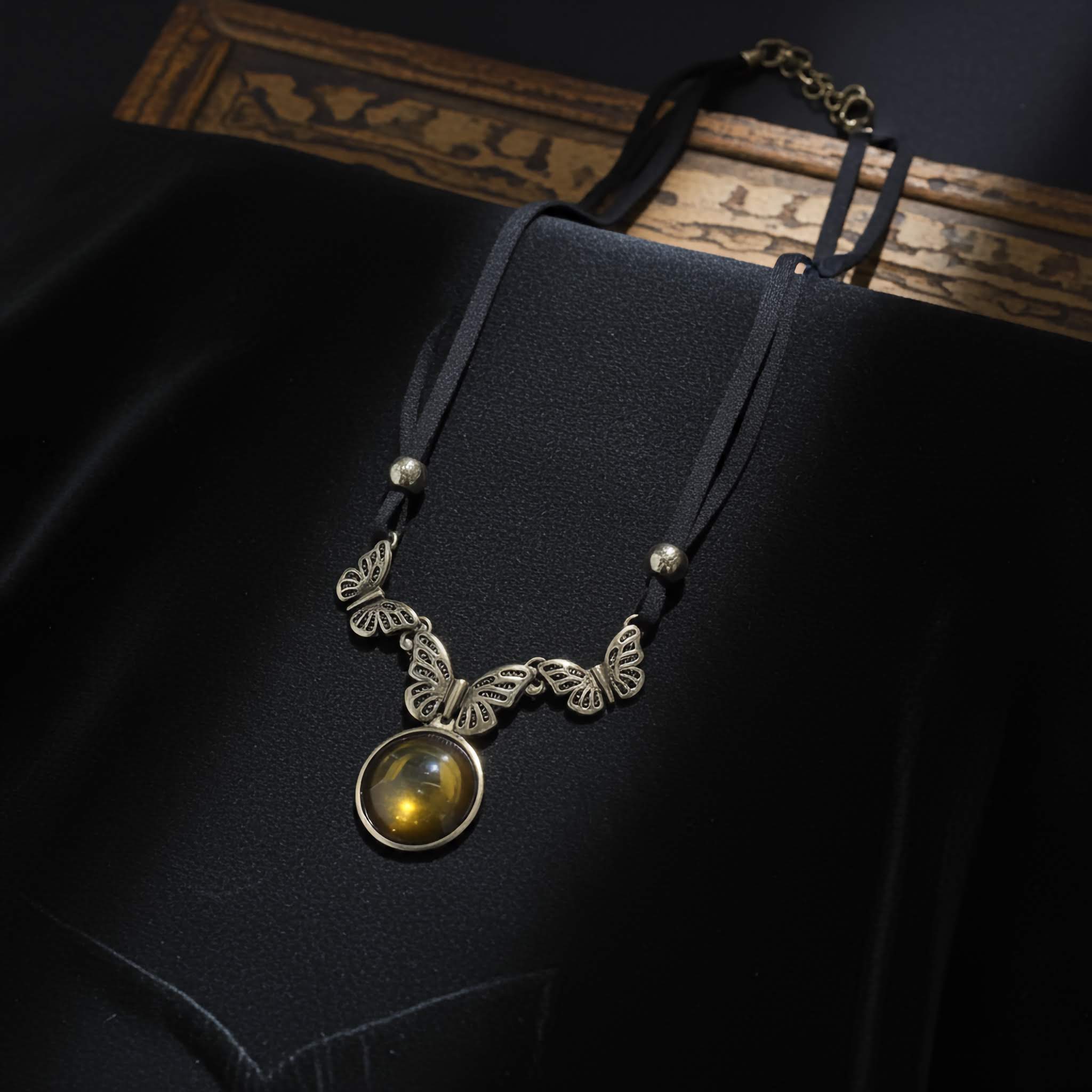 Necklace with butterfly design and yellow gemstone on a dark fabric background