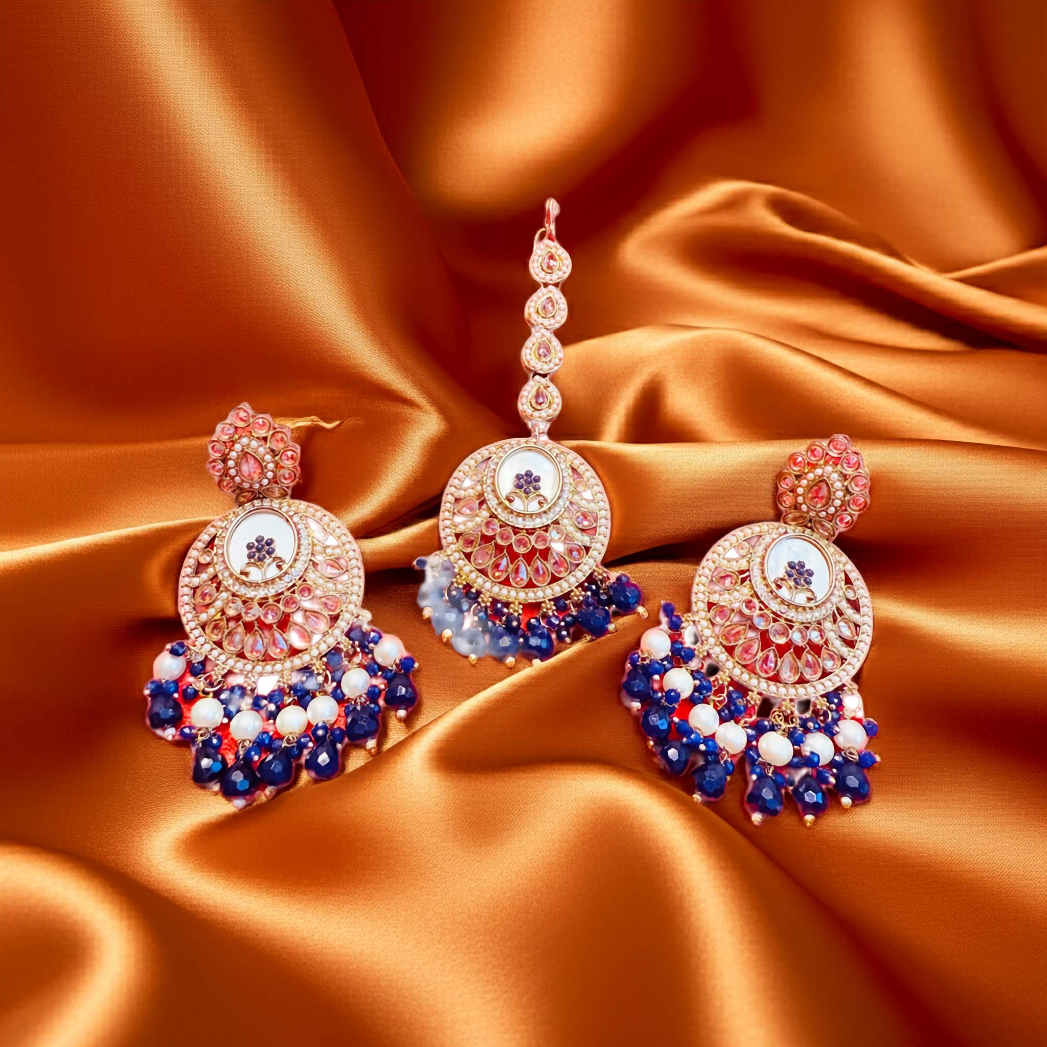 Ornate mirror work earrings and tikka with blue and pink stones on a satin background