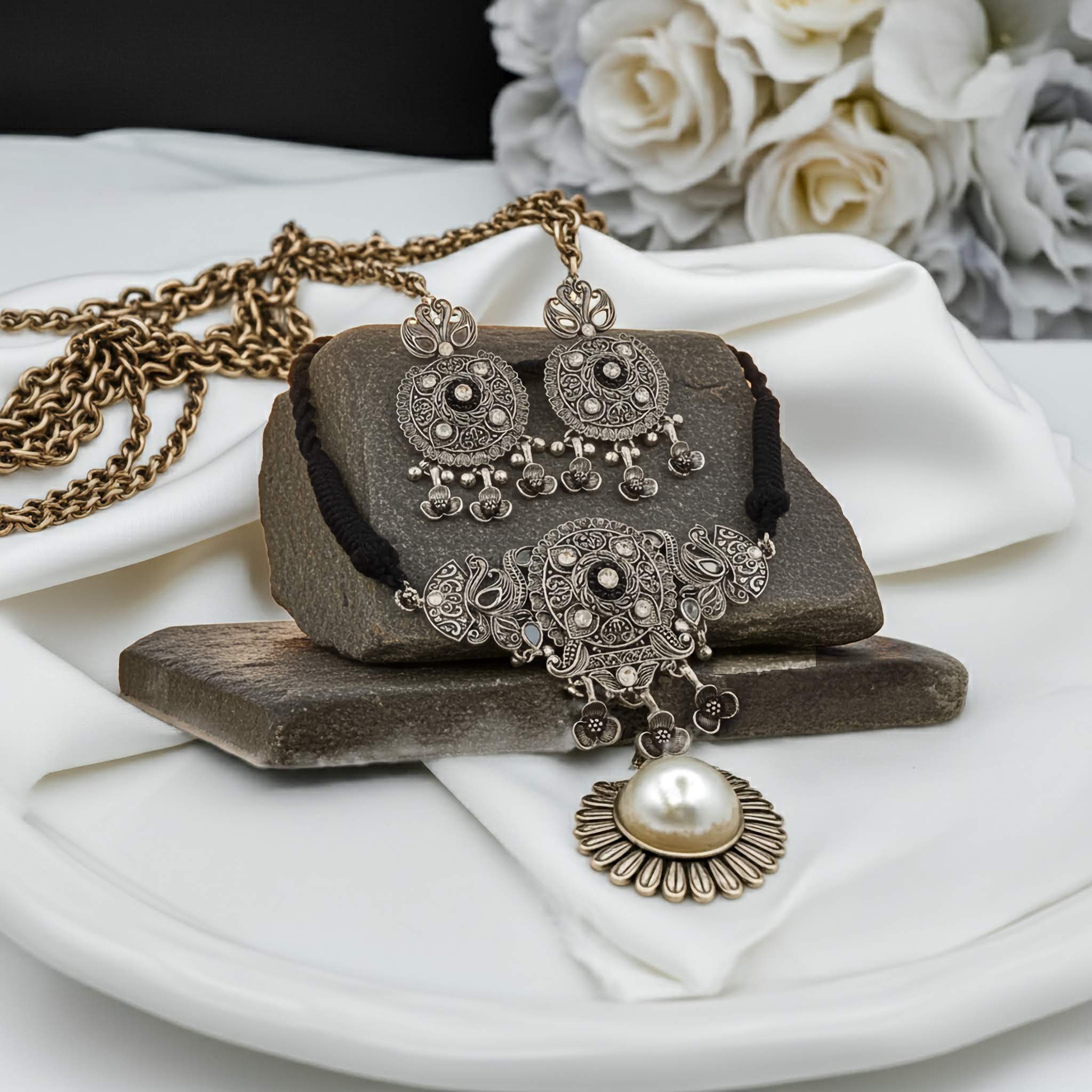 Oxidized choker with black flower charmas on a stone and white fabric.