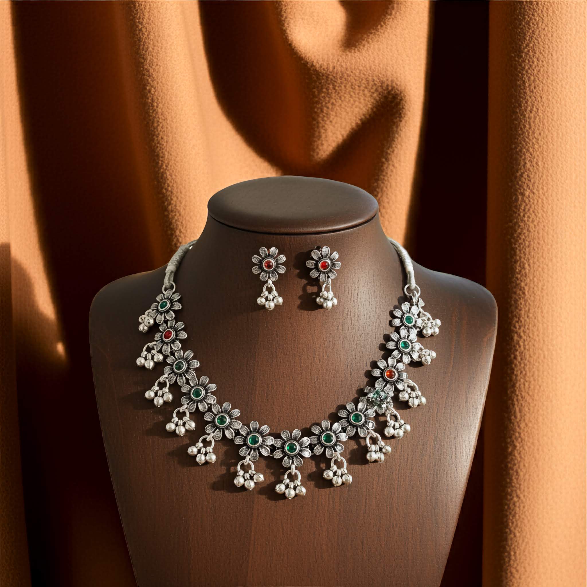 Silver oxidized necklace and earrings on a mannequin bust with an orange curtain background