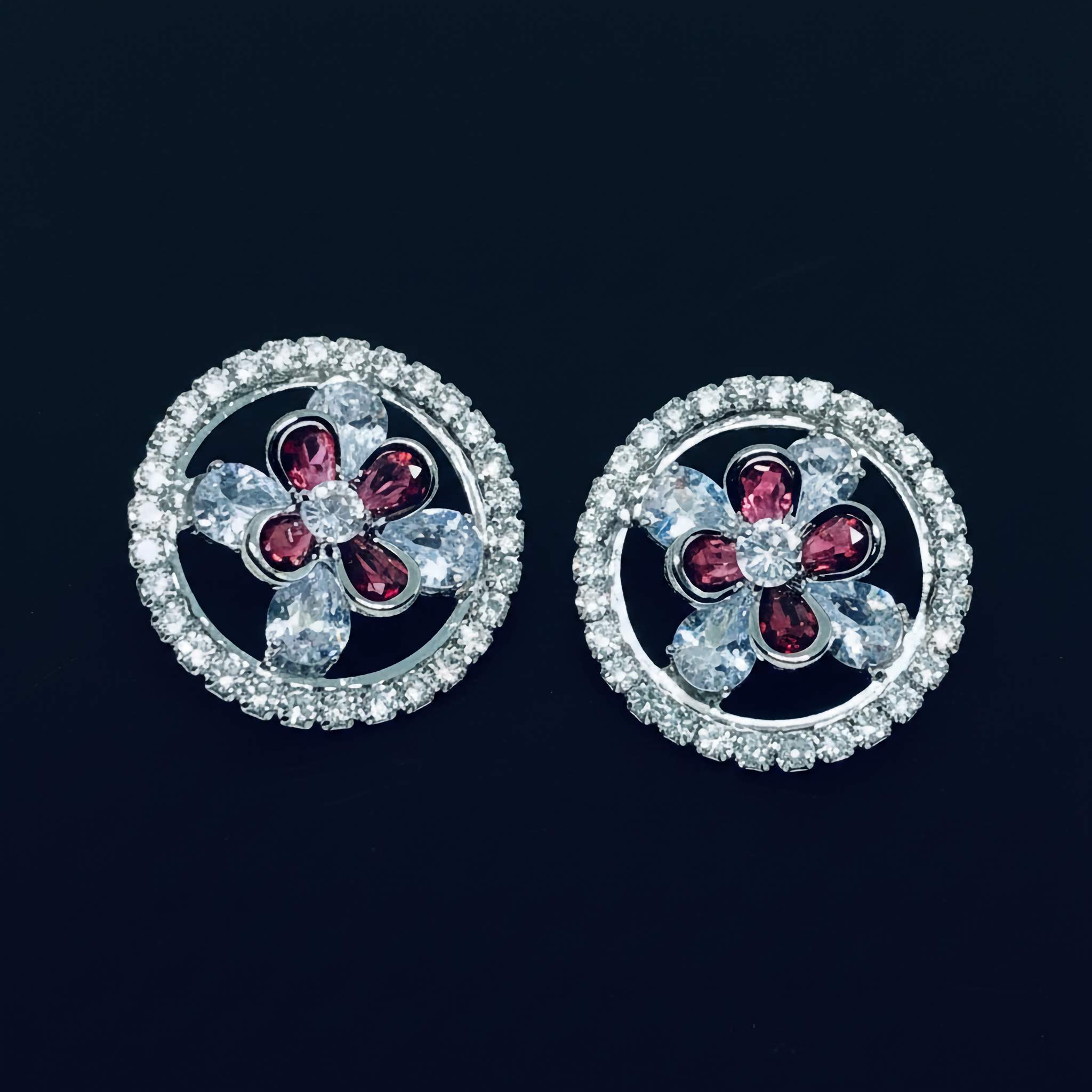 A Pair of earrings with floral design and red gemstones on a black background