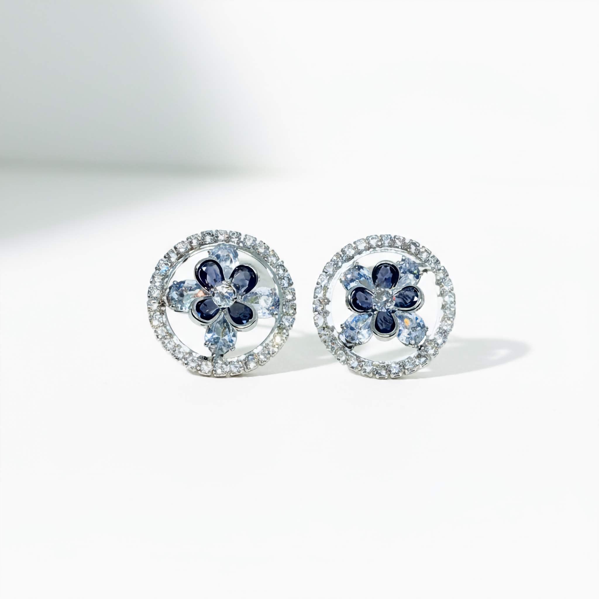 A Pair of floral stud earrings with blue and clear stones on a white background