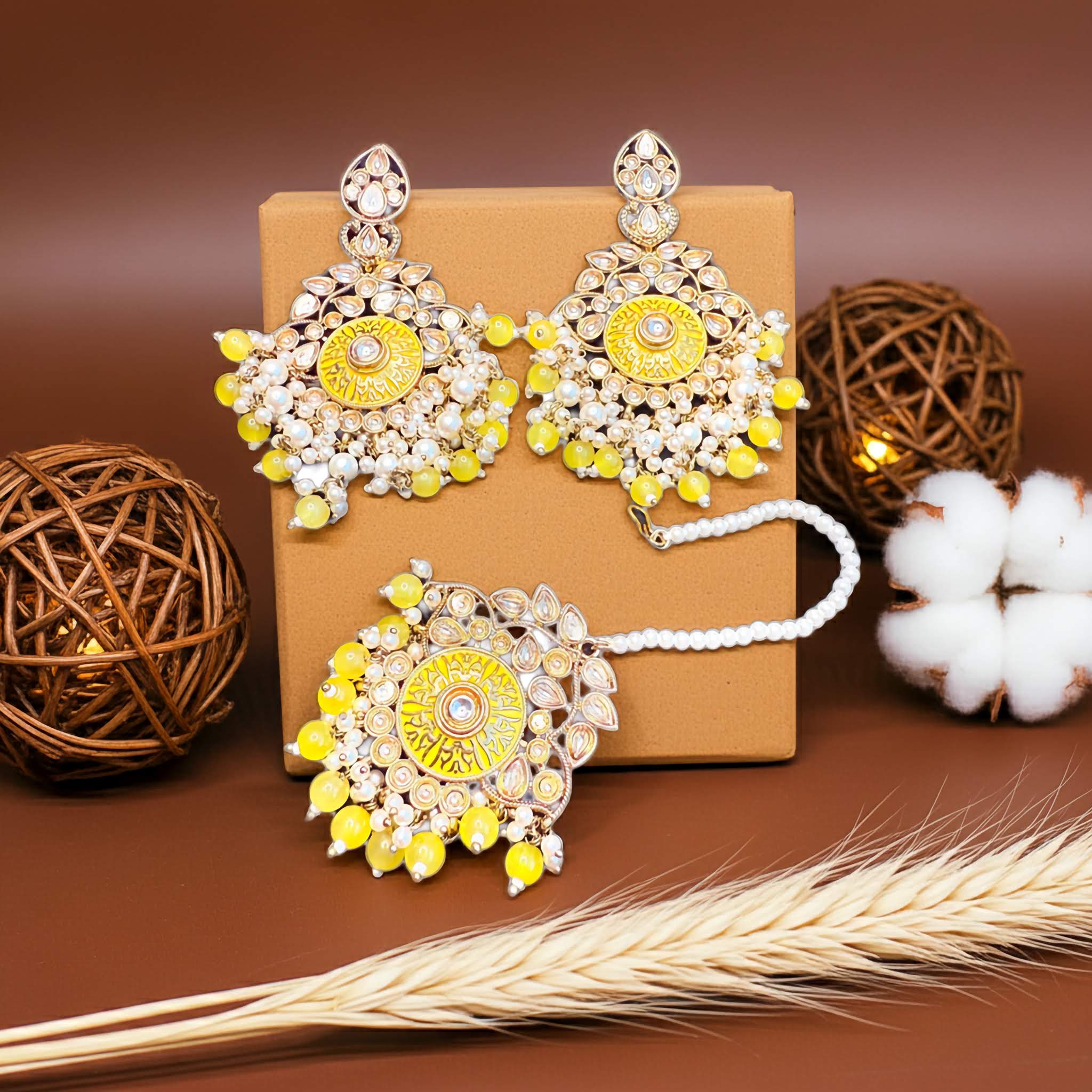 Pair of gold and yellow earrings and tikka on a brown box with decorative elements.