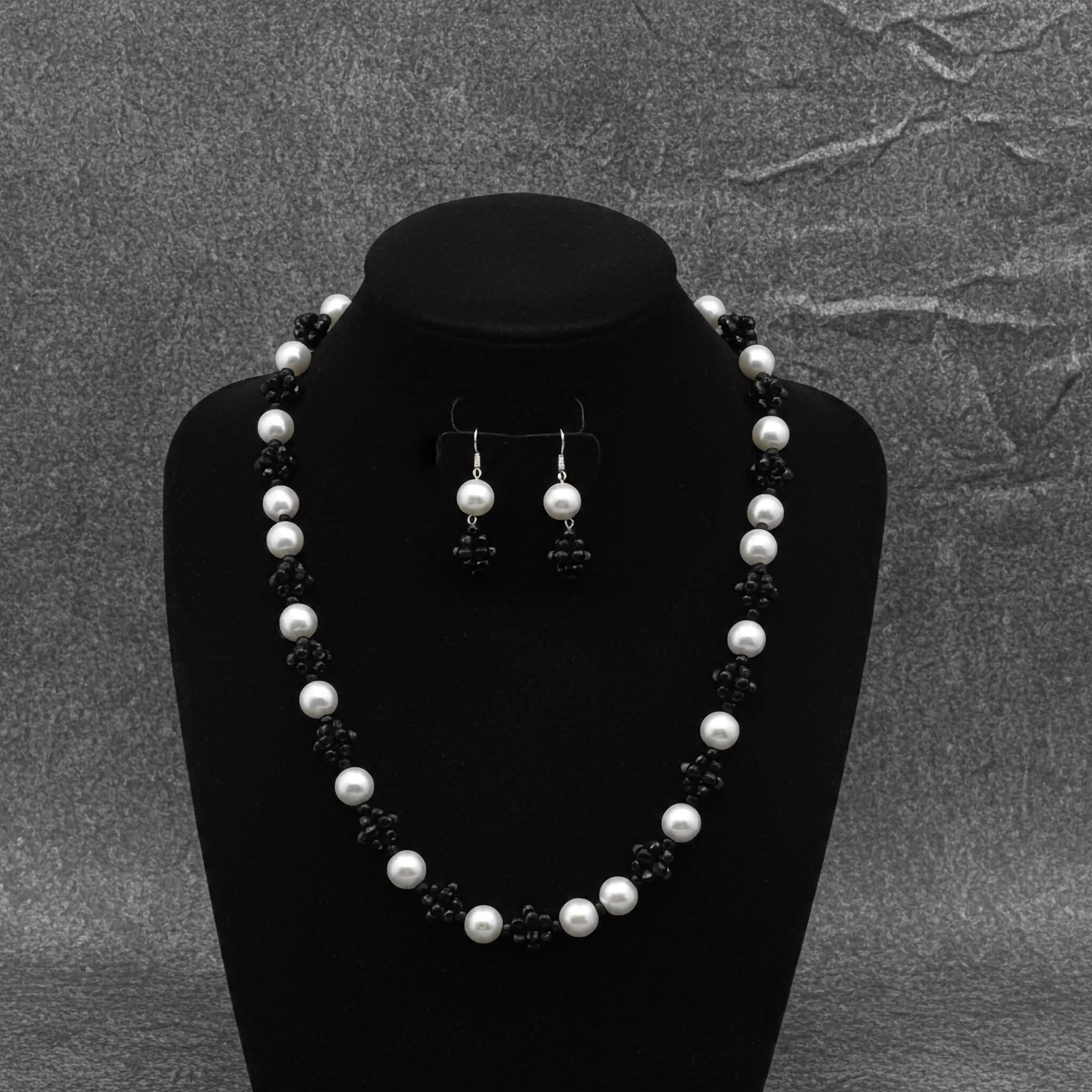Pearl necklace and earrings set on a black bust against a gray textured background