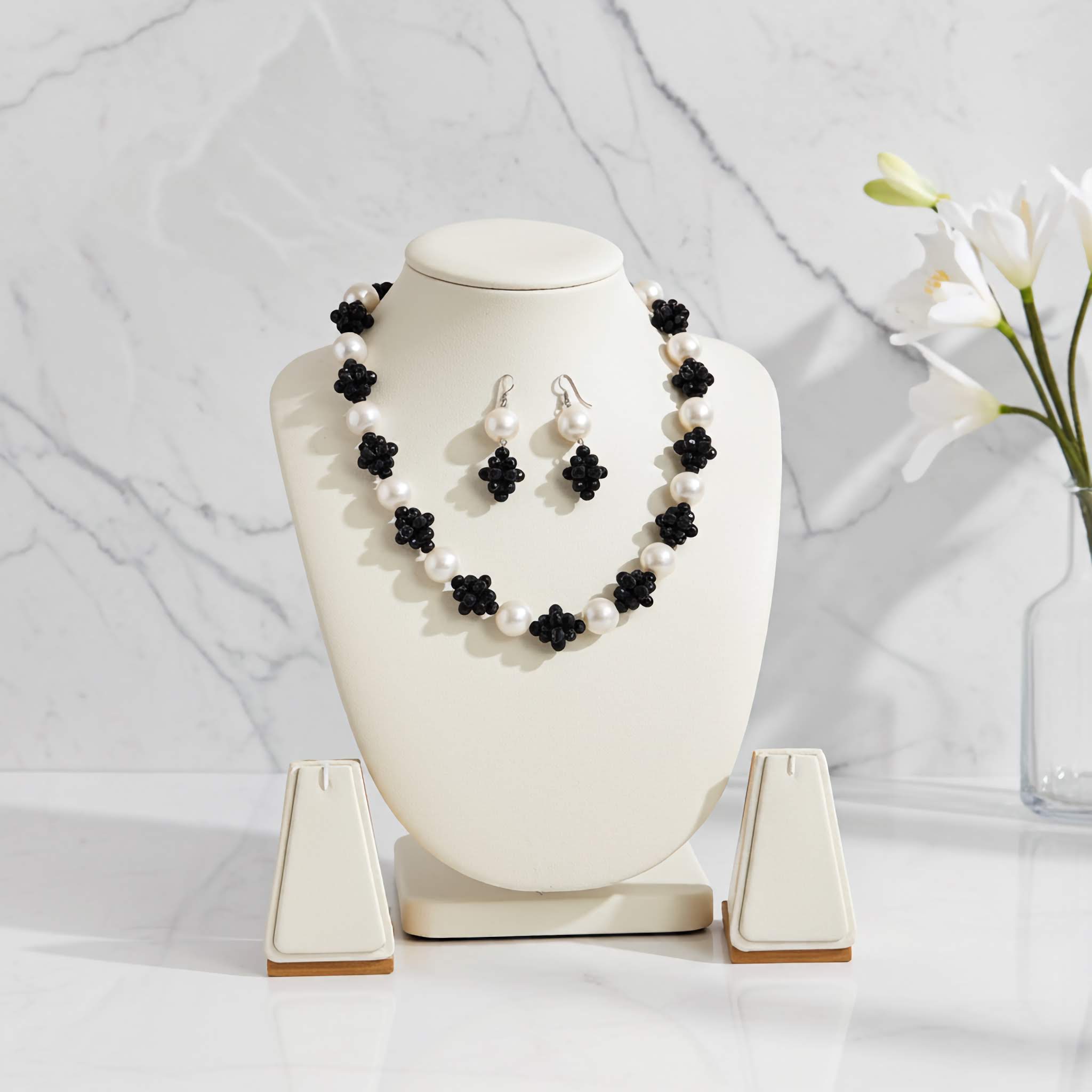 Pearl necklace with black flower accents on a white mannequin bust against a marble background.