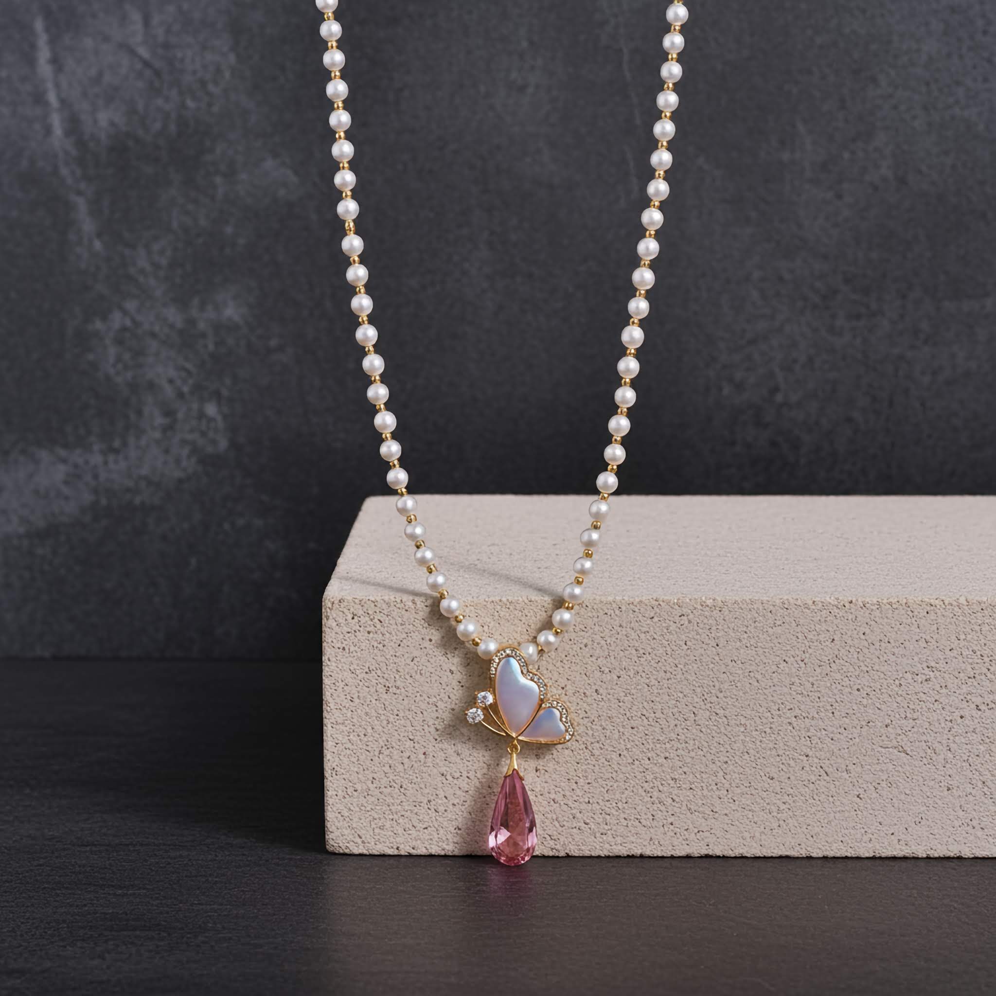 Pearl necklace with a pink teardrop pendant on a dark surface