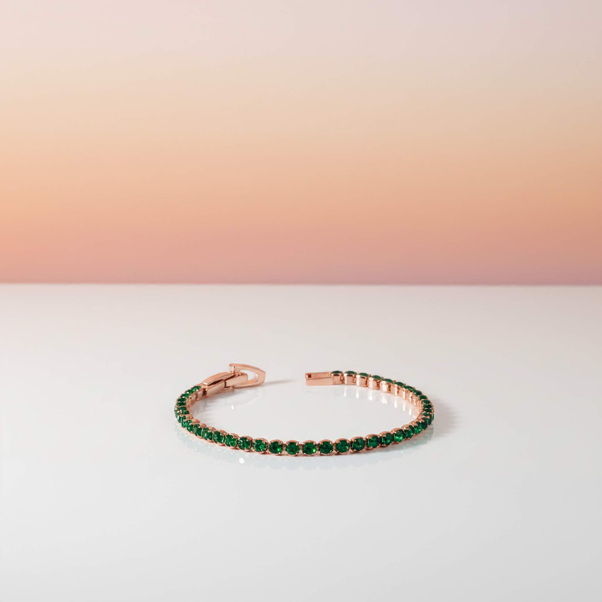Rose gold tennis bracelet with green gemstones on a gradient background
