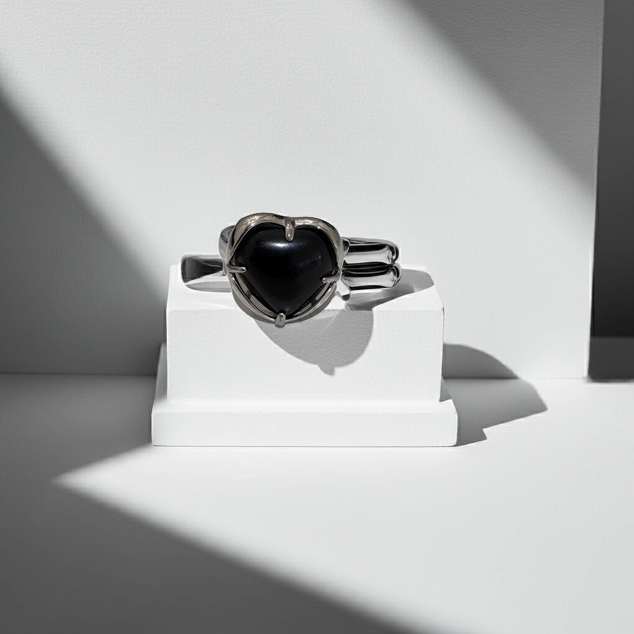 Silver ring with a black gemstone on a white stand against a light gray background