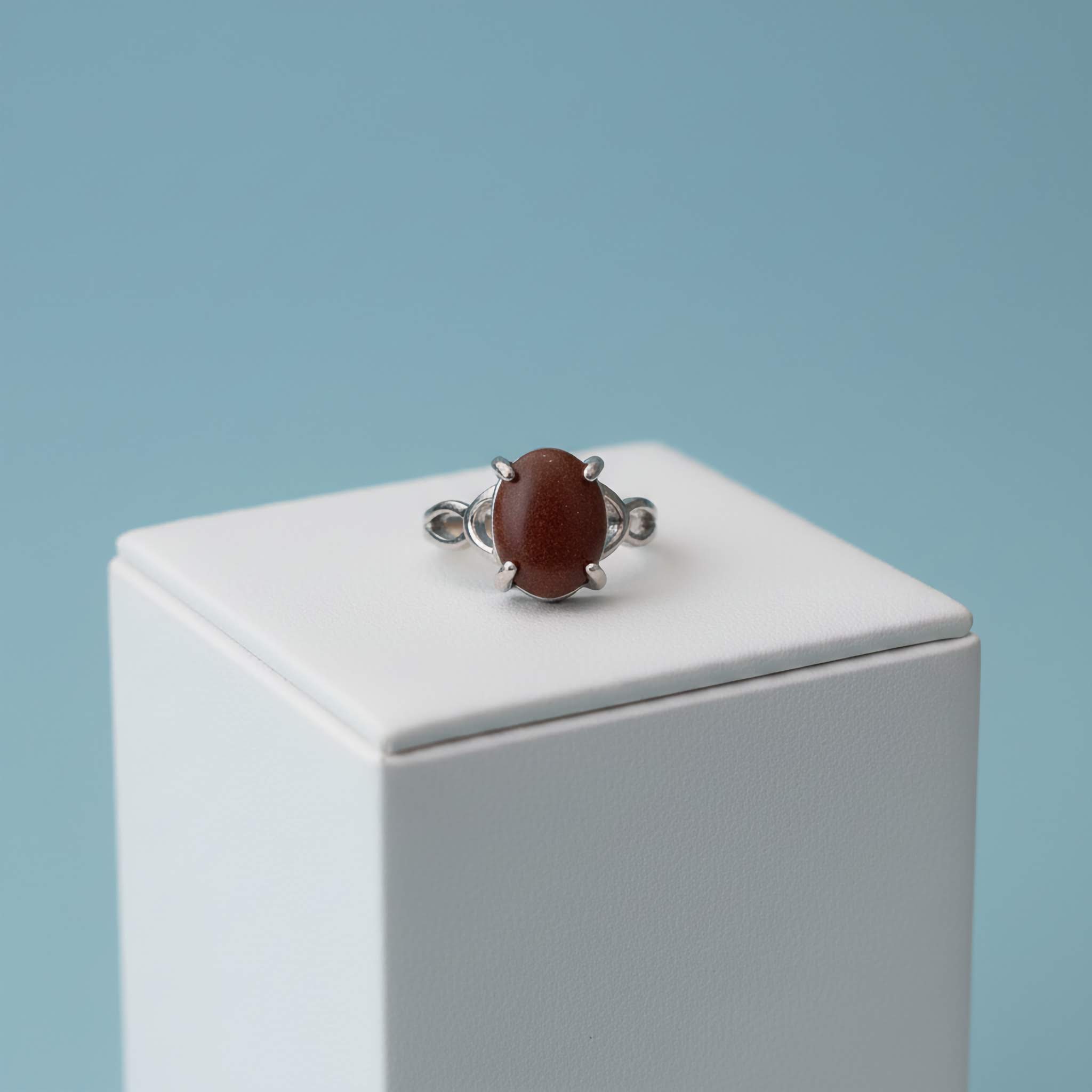 Silver ring with a brown gemstone on a white stand against a light blue background