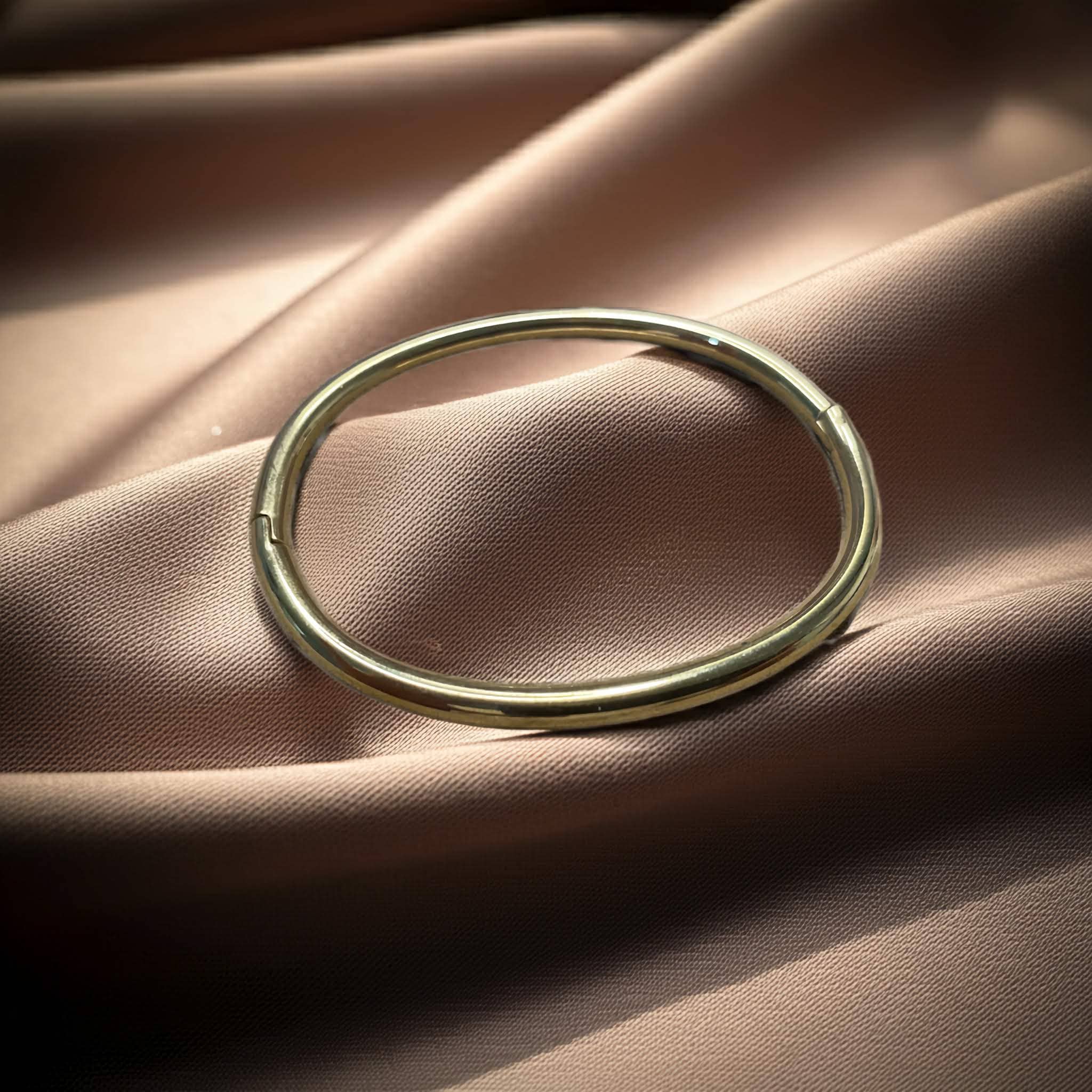 Simple Gold plated pipe bangle on a soft pink fabric background
