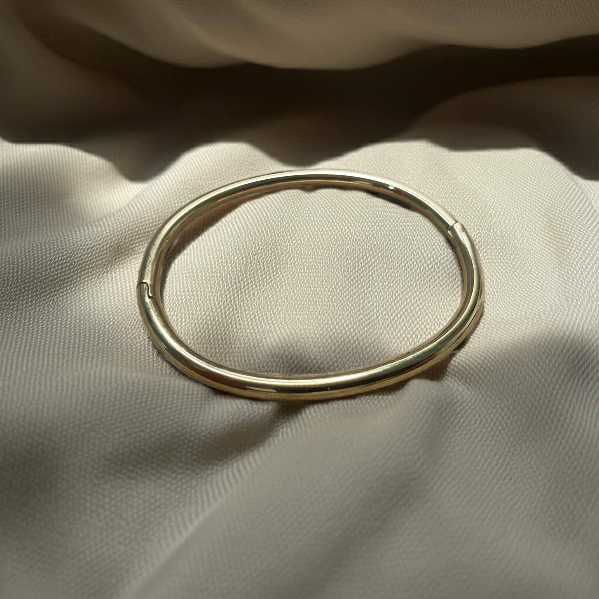 Simple pipe bangle gold plated on a beige fabric surface