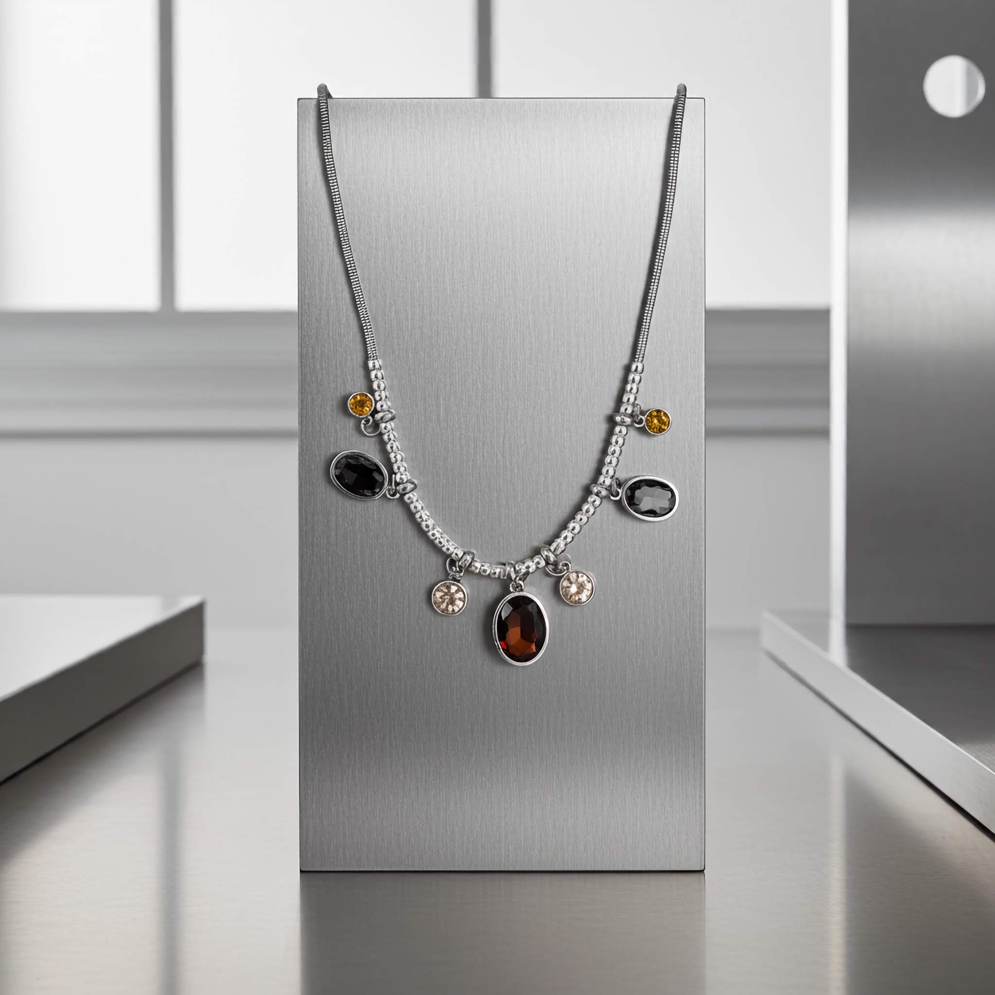 A silver plated Necklace with coloured stones on a metallic stand against a neutral background offered at $10.