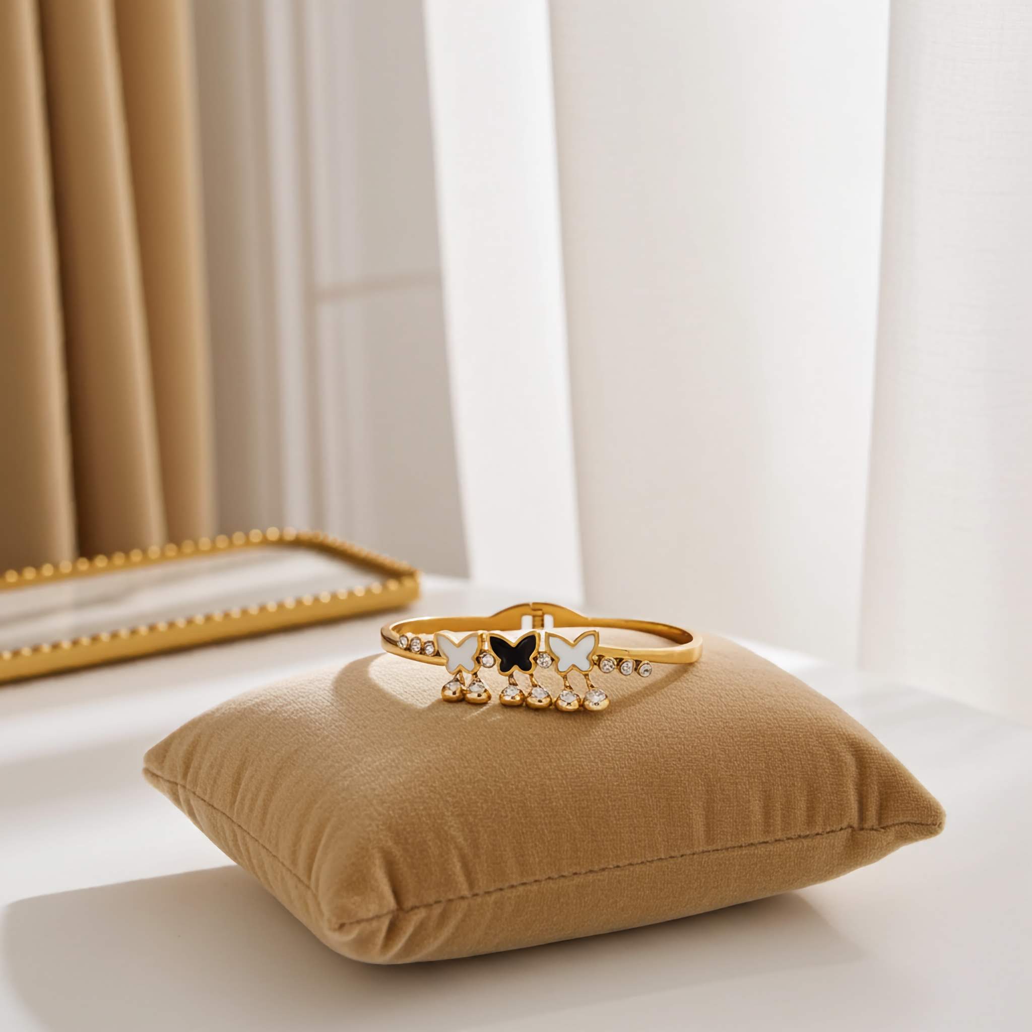 Gold bracelet with butterfly charms on a brown pillow in a softly lit room.