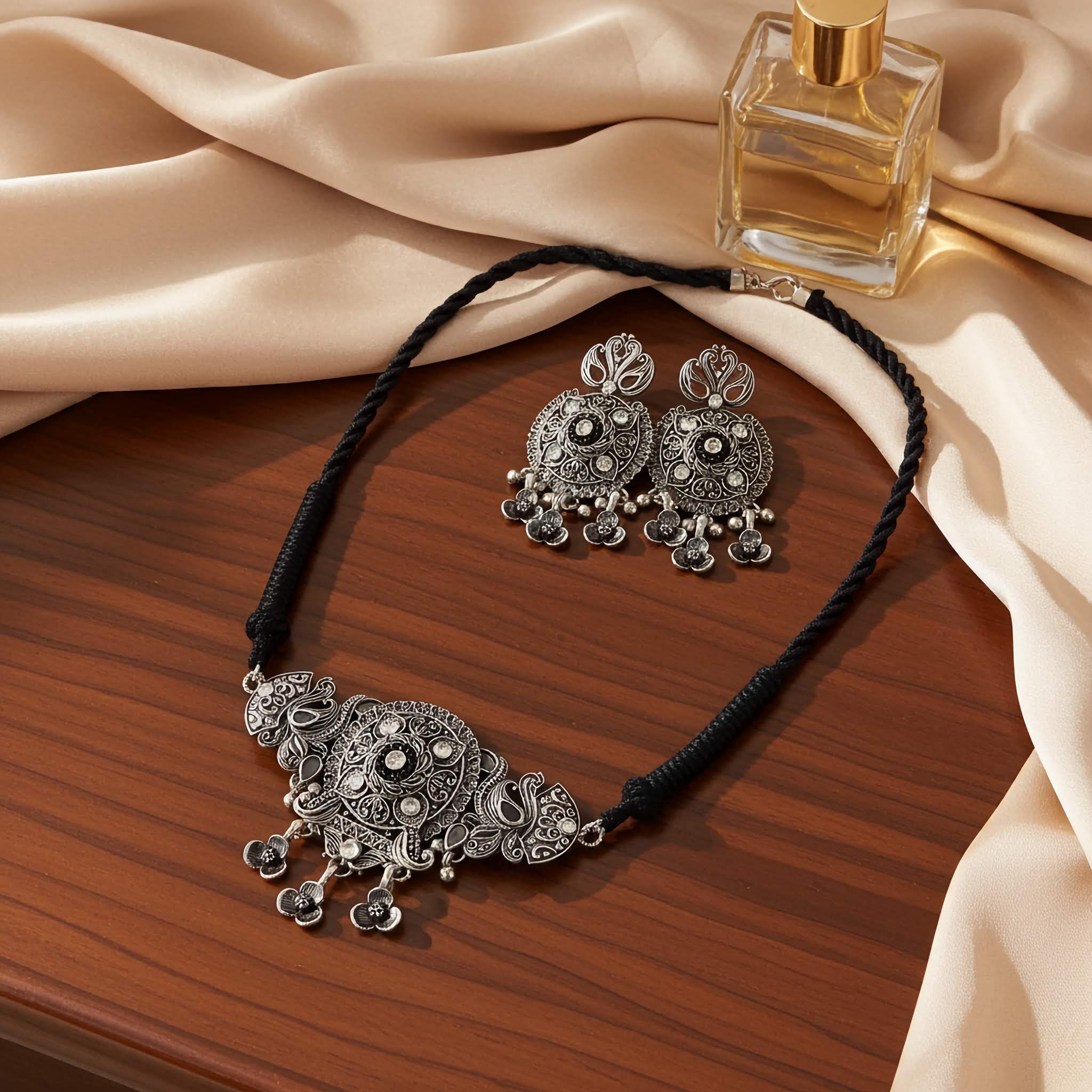 Silver necklace choker set and earrings on a wooden surface with a perfume bottle.