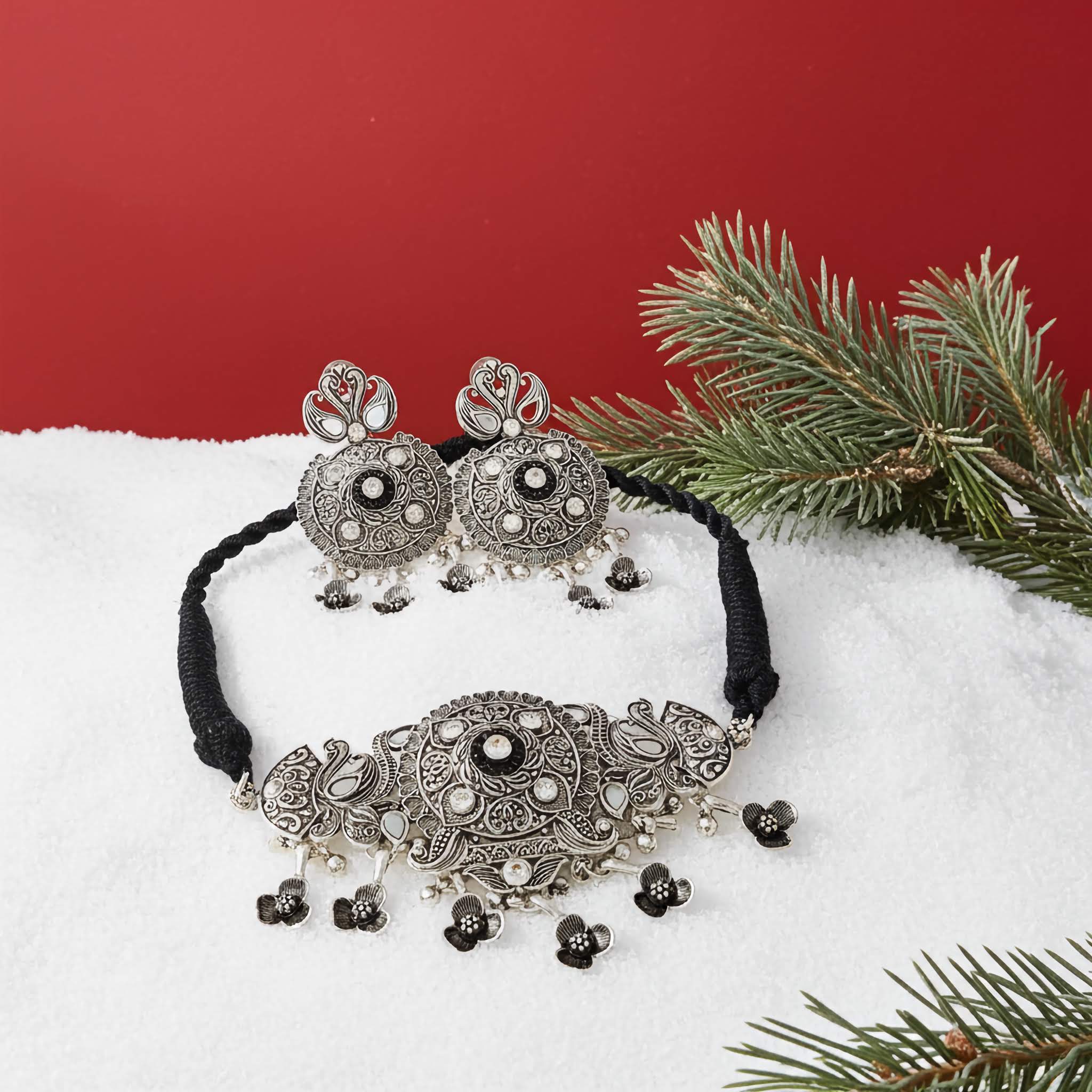 Silver jewelry choker set with black cord oand earrings on a snowy surface with Christmas tree branches.