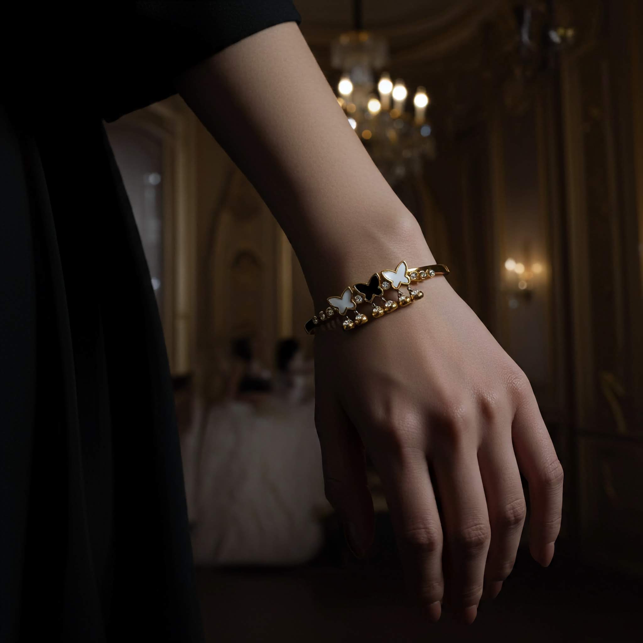 Hand wearing a gold bracelet with star and butterfly designs in an elegant indoor setting.