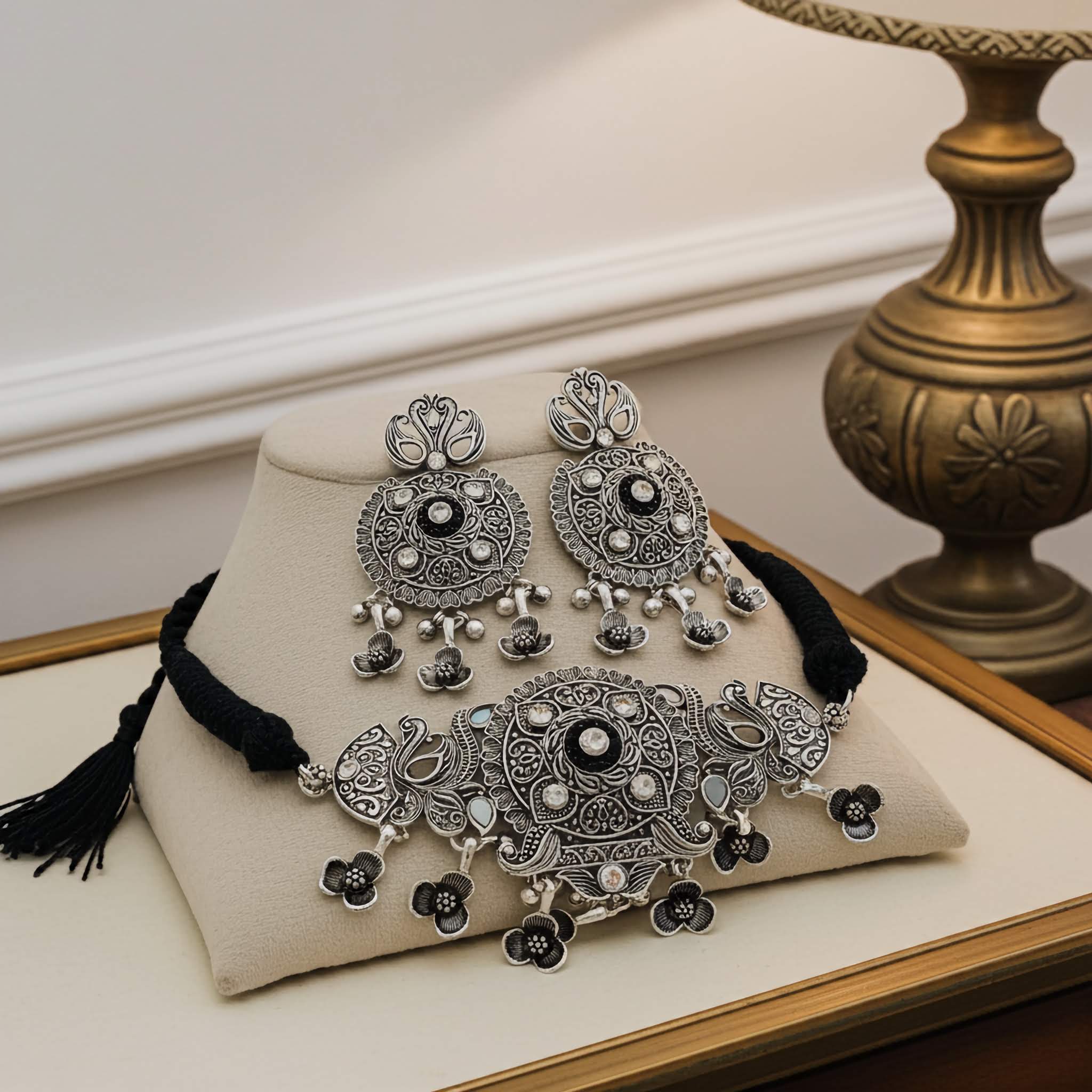 Ornate silver necklace and earrings set on a beige pillow with a decorative background.