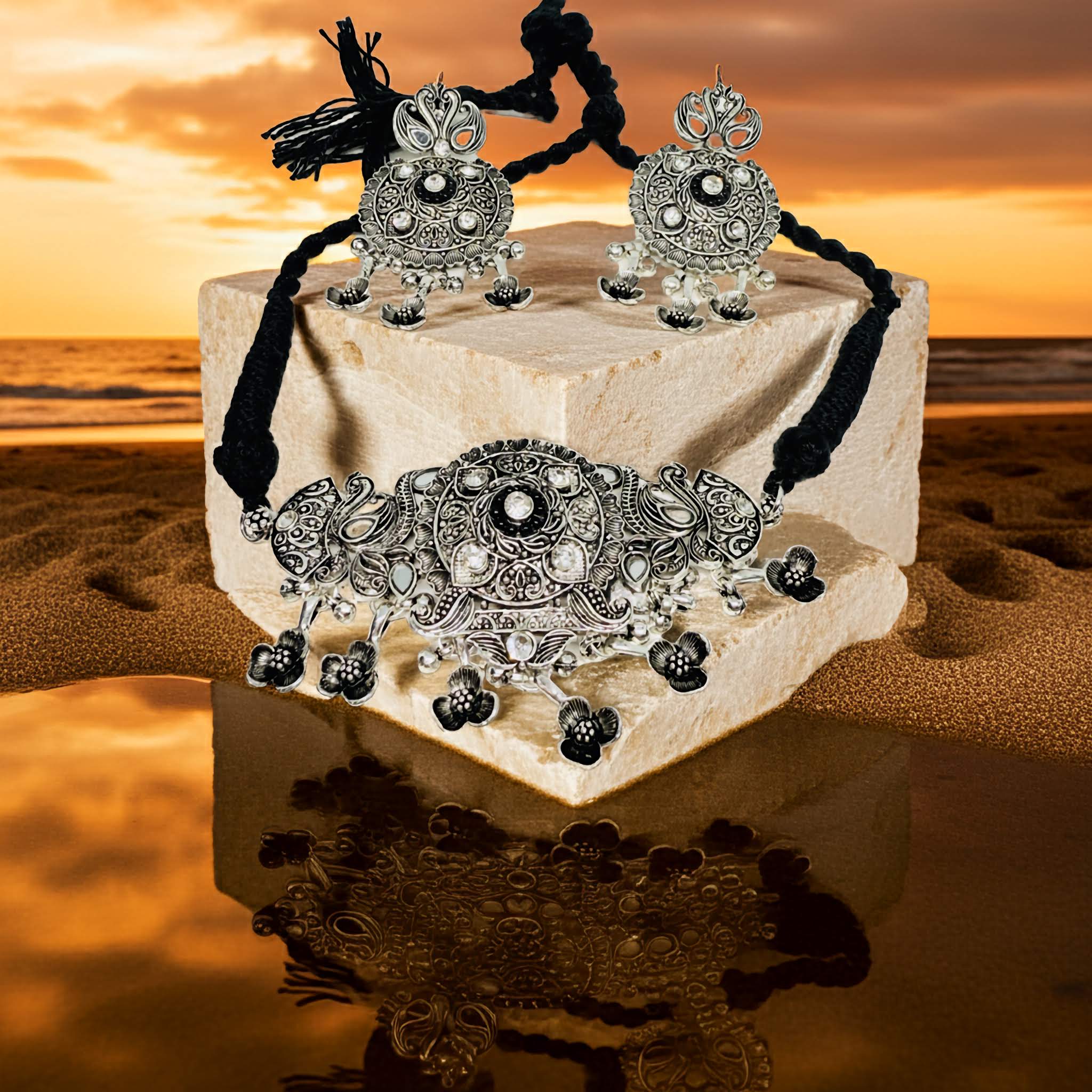 Ornate silver necklace and earrings on a reflective surface with a sunset background