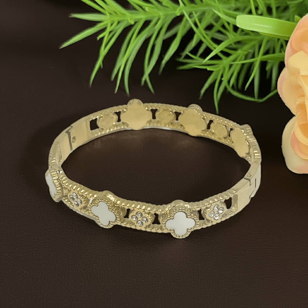 White clover Gold bangle with floral designs on a dark surface with green leaves and a flower in the background