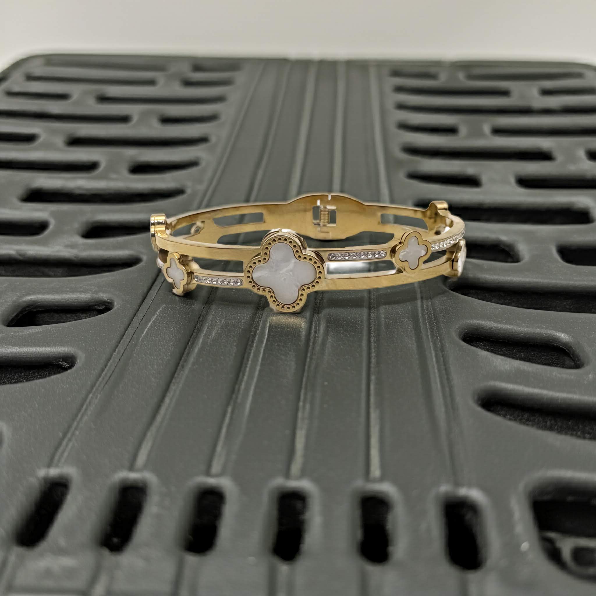 Gold bracelet with clover design on a textured black surface