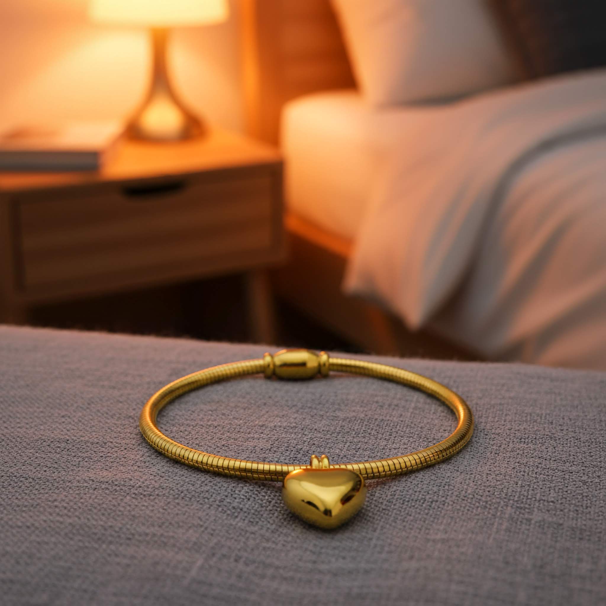 A Dainty Gold bracelet with a heart charm on a textured surface, blurred background of a cozy room.
