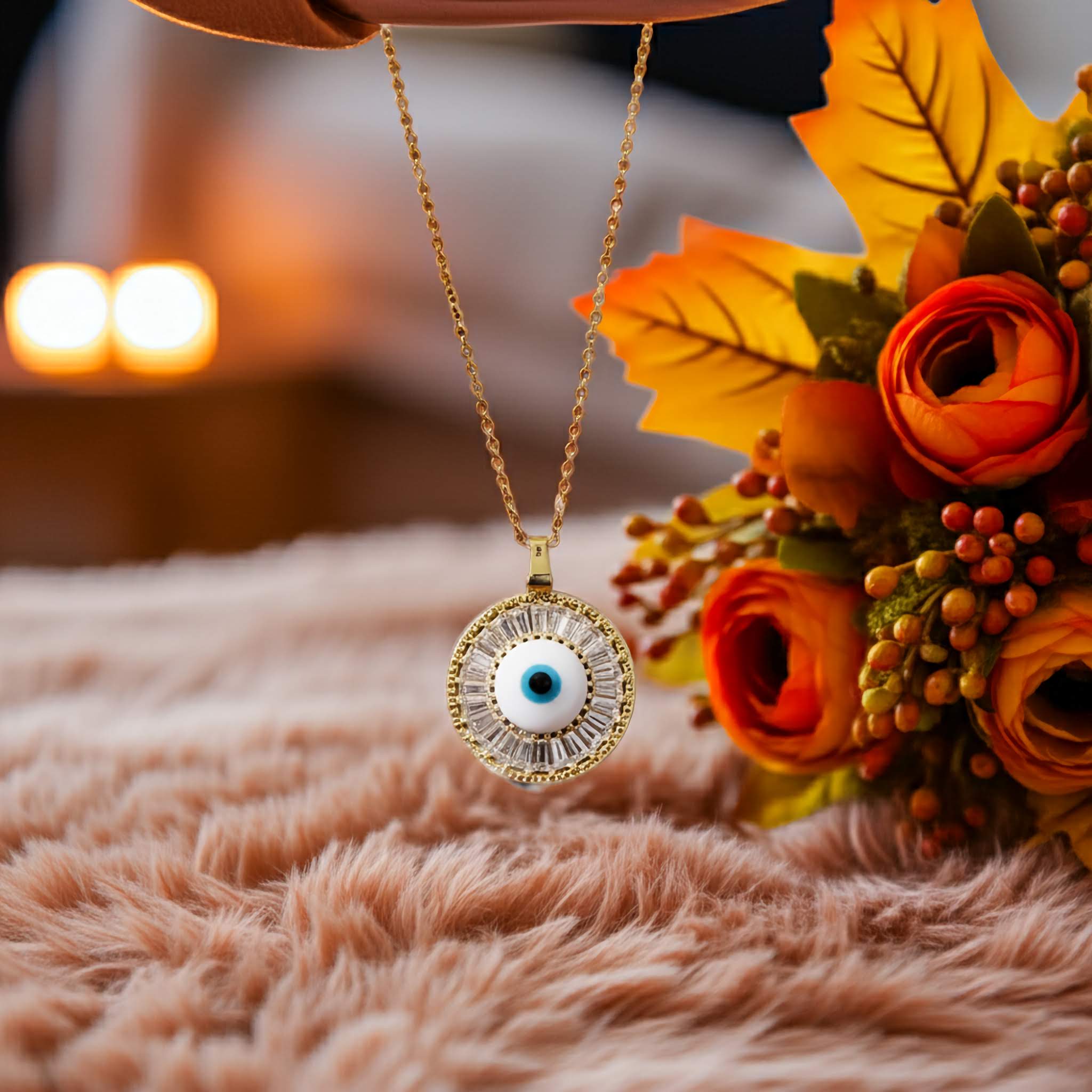 A gold evil eye Necklace with an eye pendant on a soft surface with autumn leaves and flowers.