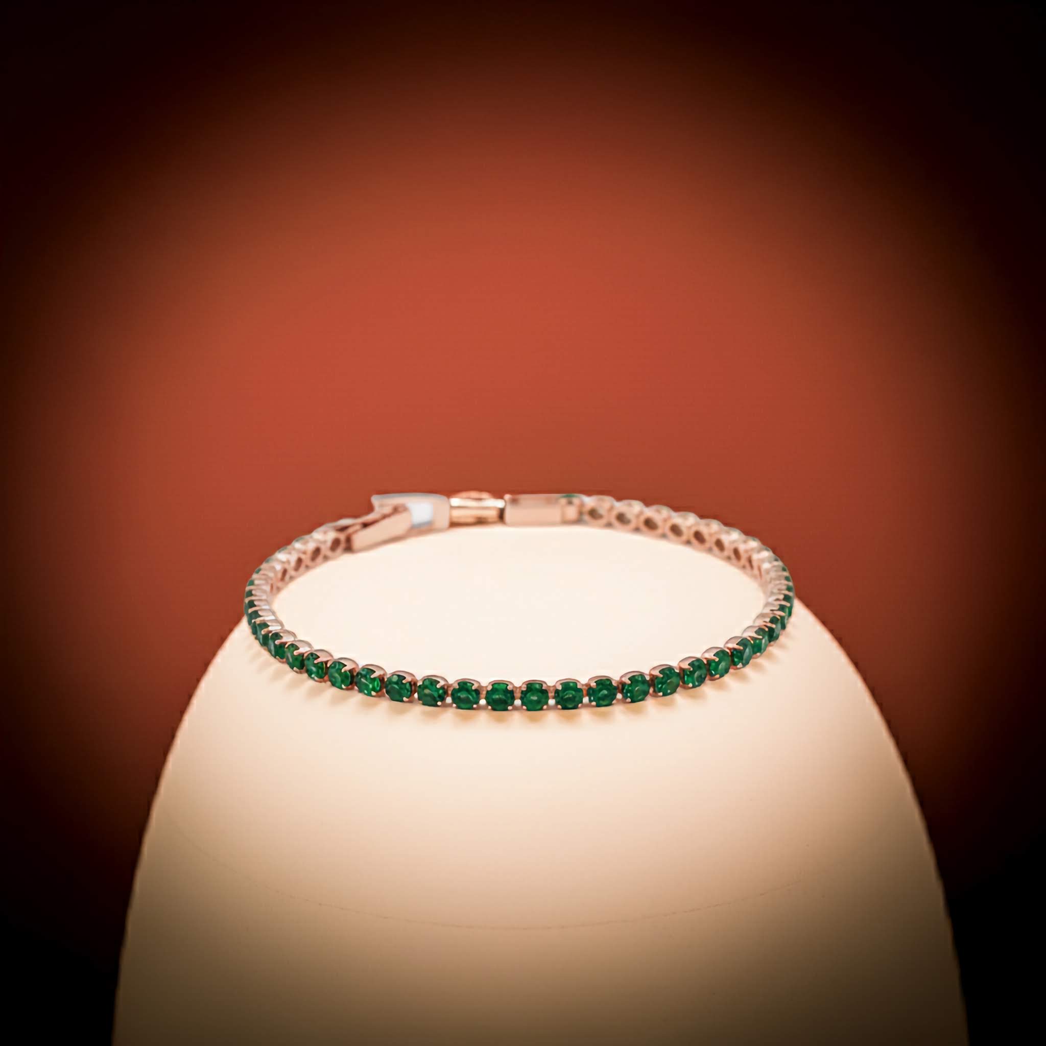 Tennis Bracelet with green gemstones on a white stand against a dark background