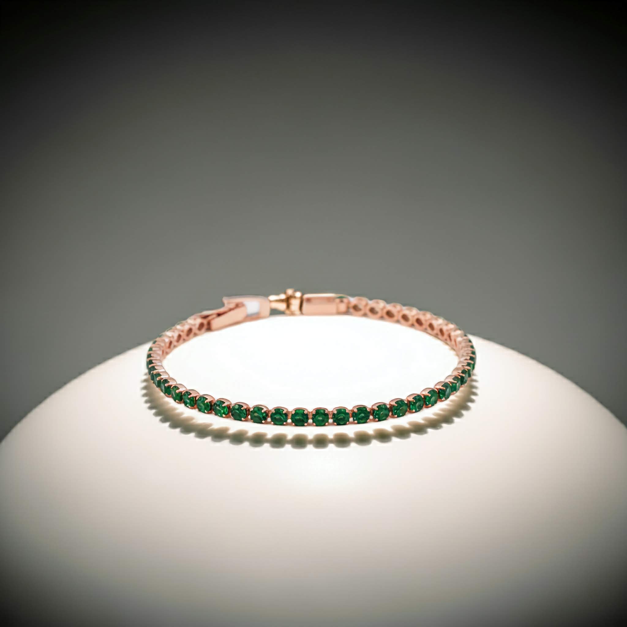 Rose gold tennis bracelet with green gemstones on a gray background