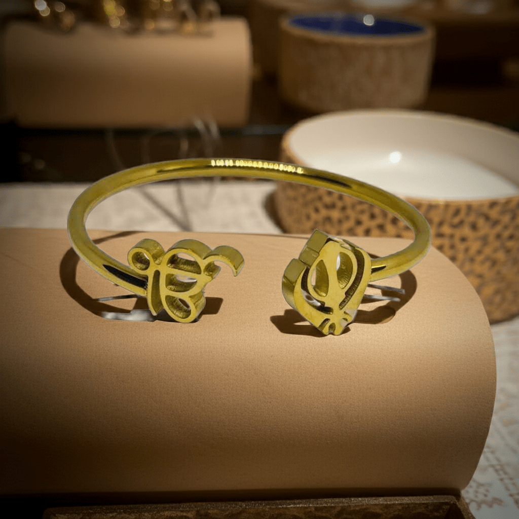 Gold bracelet of ik onkar and khanda symbols on a beige cushion with blurred background
