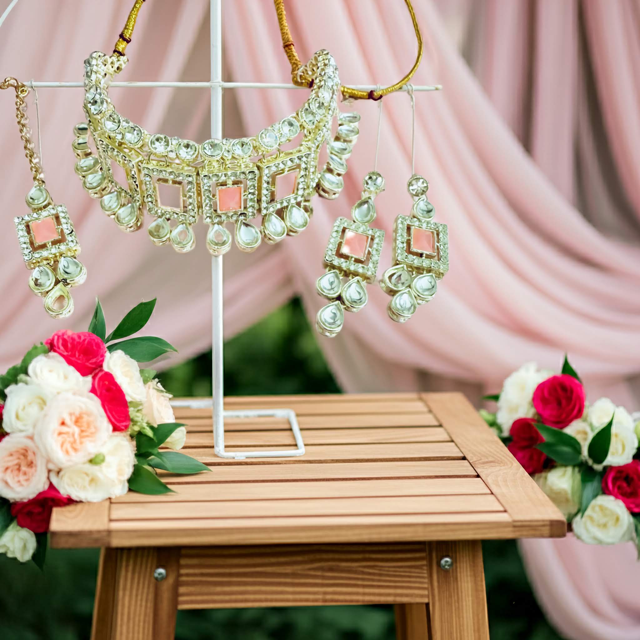 Silver choker kundan Jewelry set with necklace and earrings on a stand, surrounded by flowers and pink fabric.