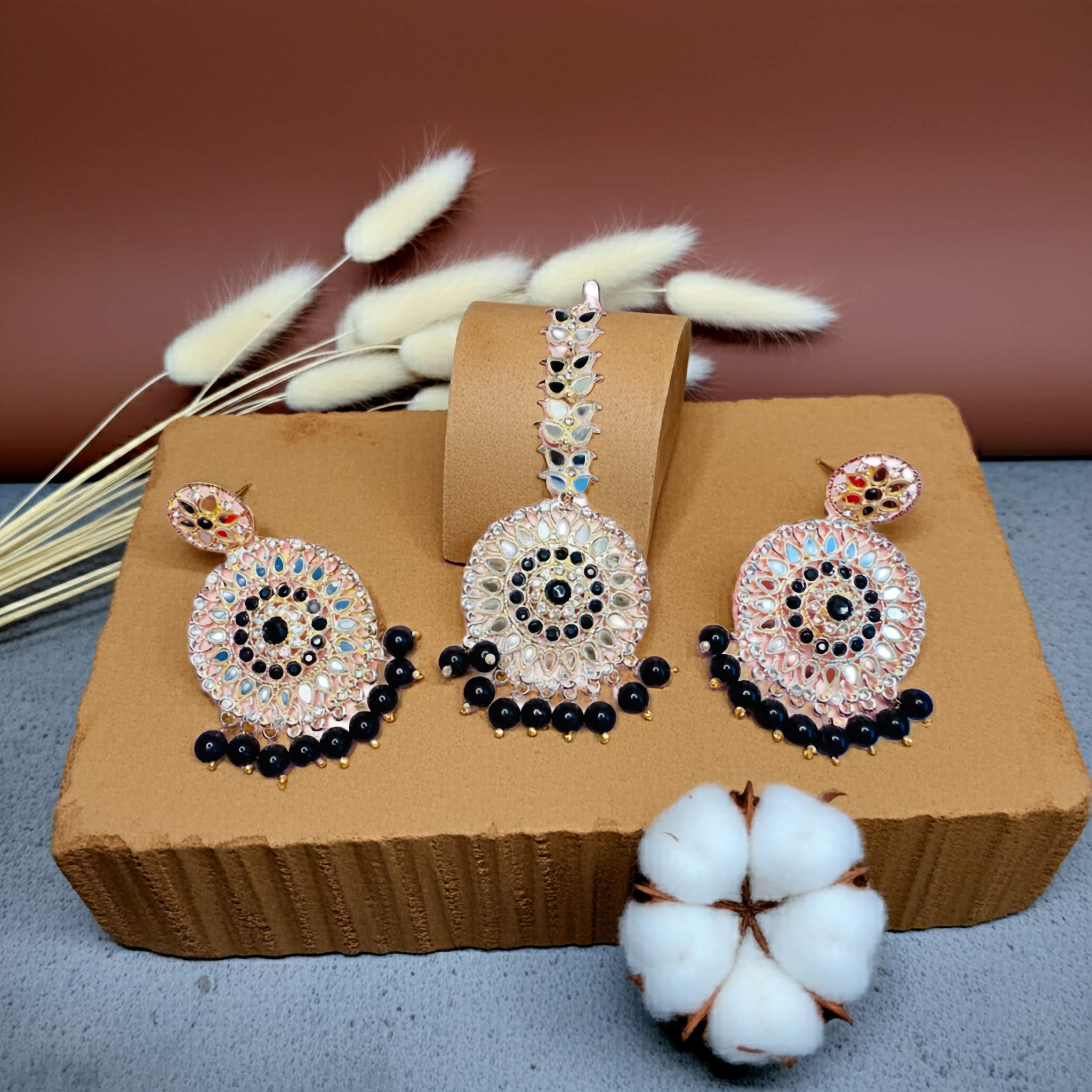 Ornate mirror work earrings and tikka with purple and pink gemstones on a brown box with a neutral background
