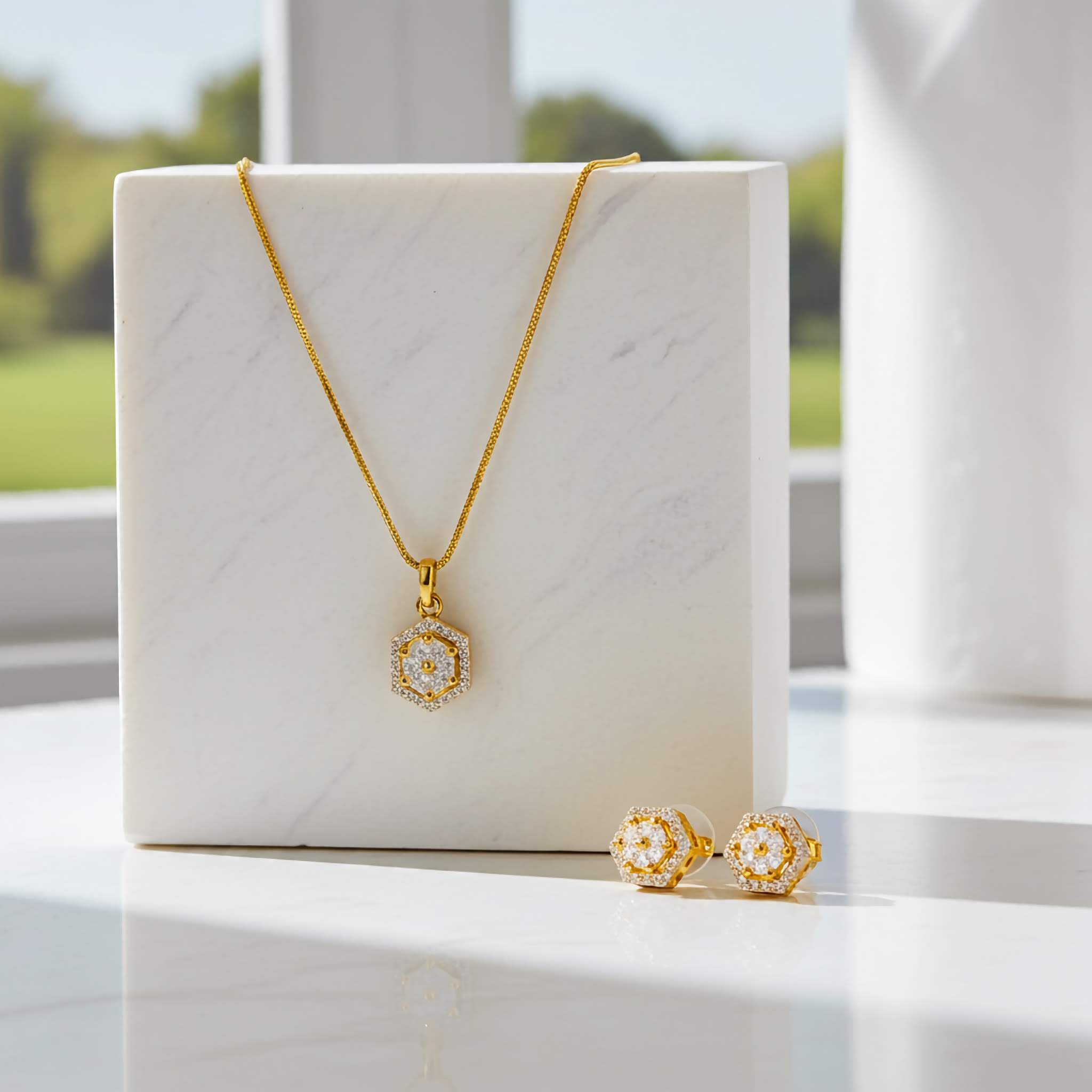 Zirconia jewelry set of 18k Gold plated necklace and earrings on a marble surface with a blurred outdoor background