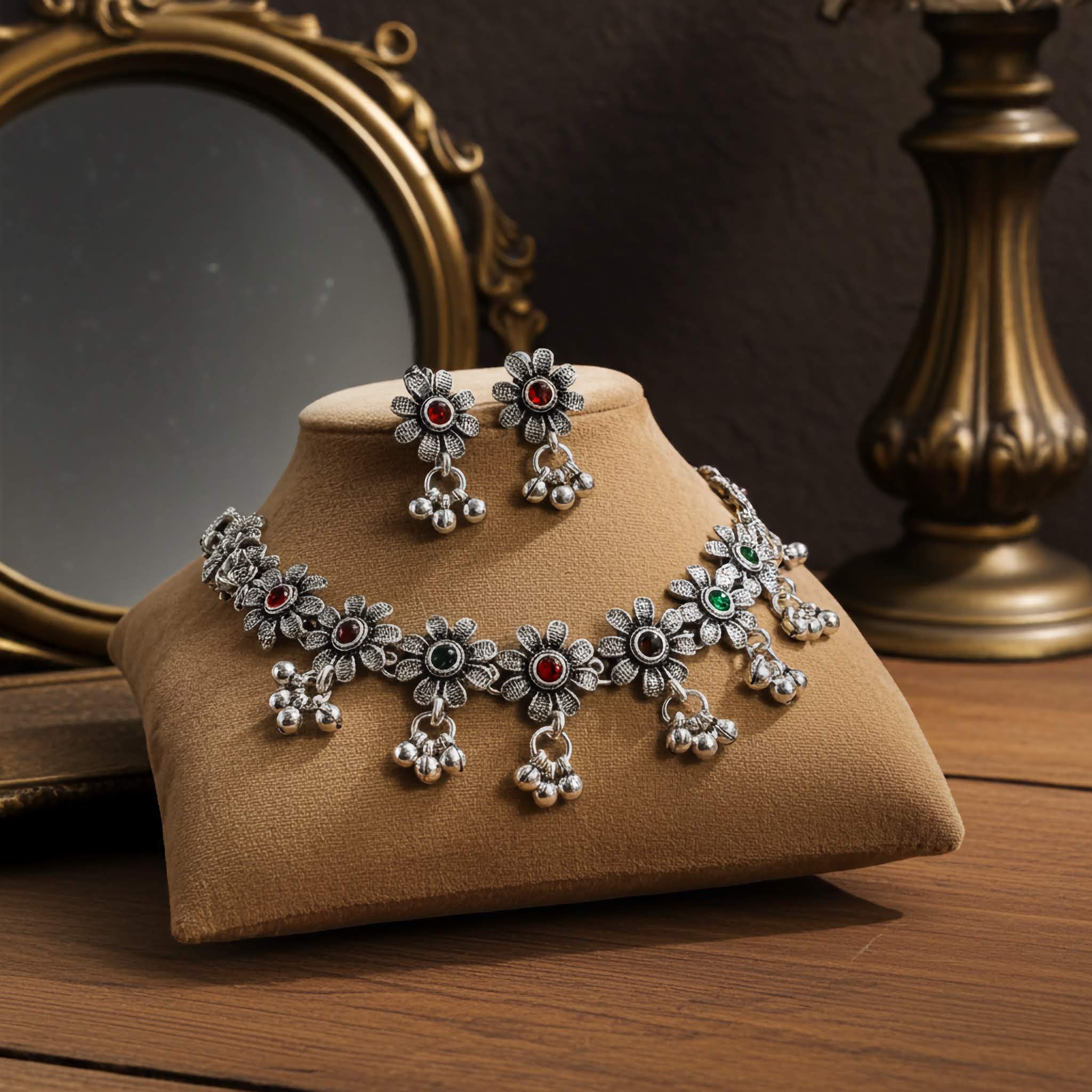 Silver oxidized Jewelry set with necklace and earrings on a brown cushion, with a reflective surface and gold lamp in the background.