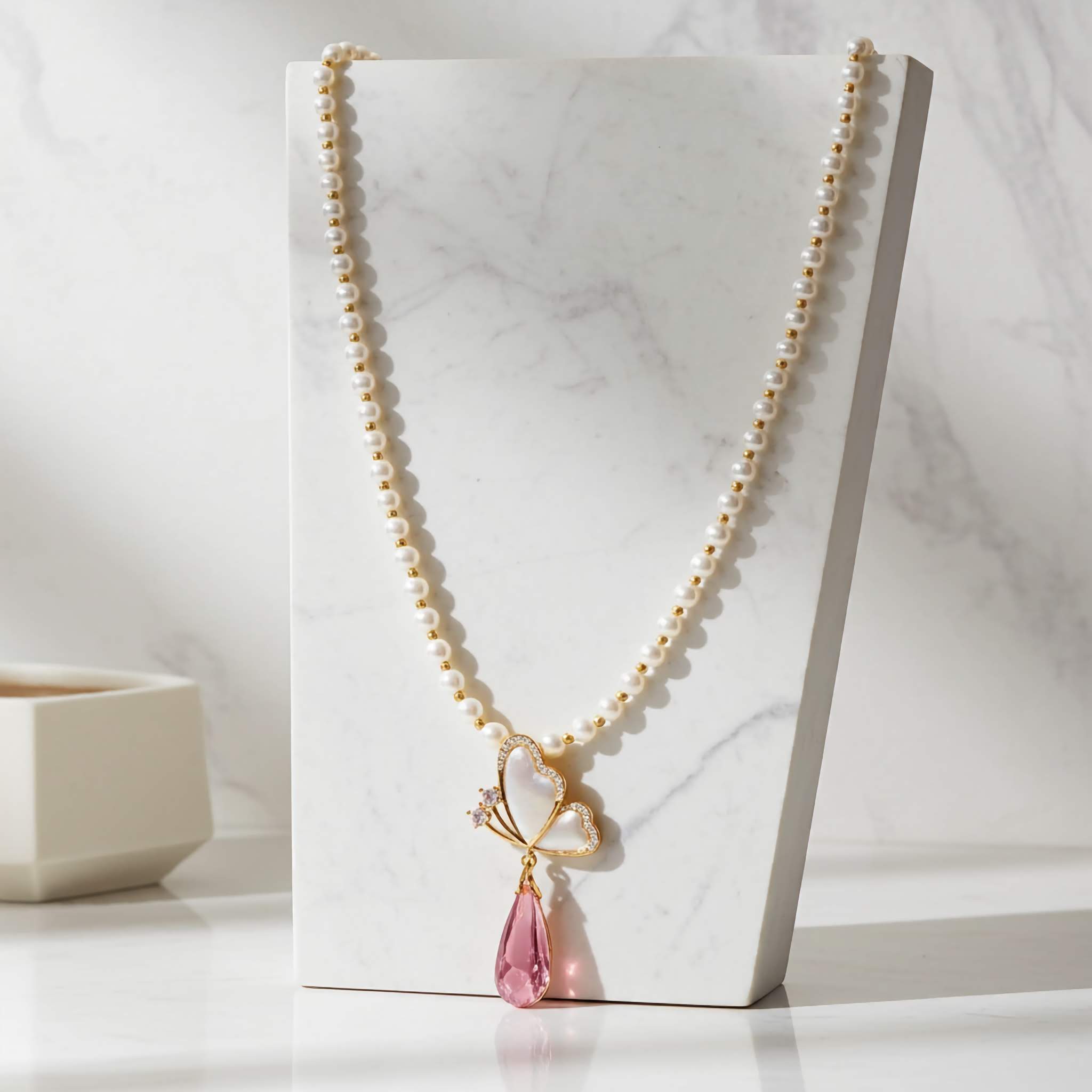 Pearl necklace with a pink teardrop pendant on a marble surface