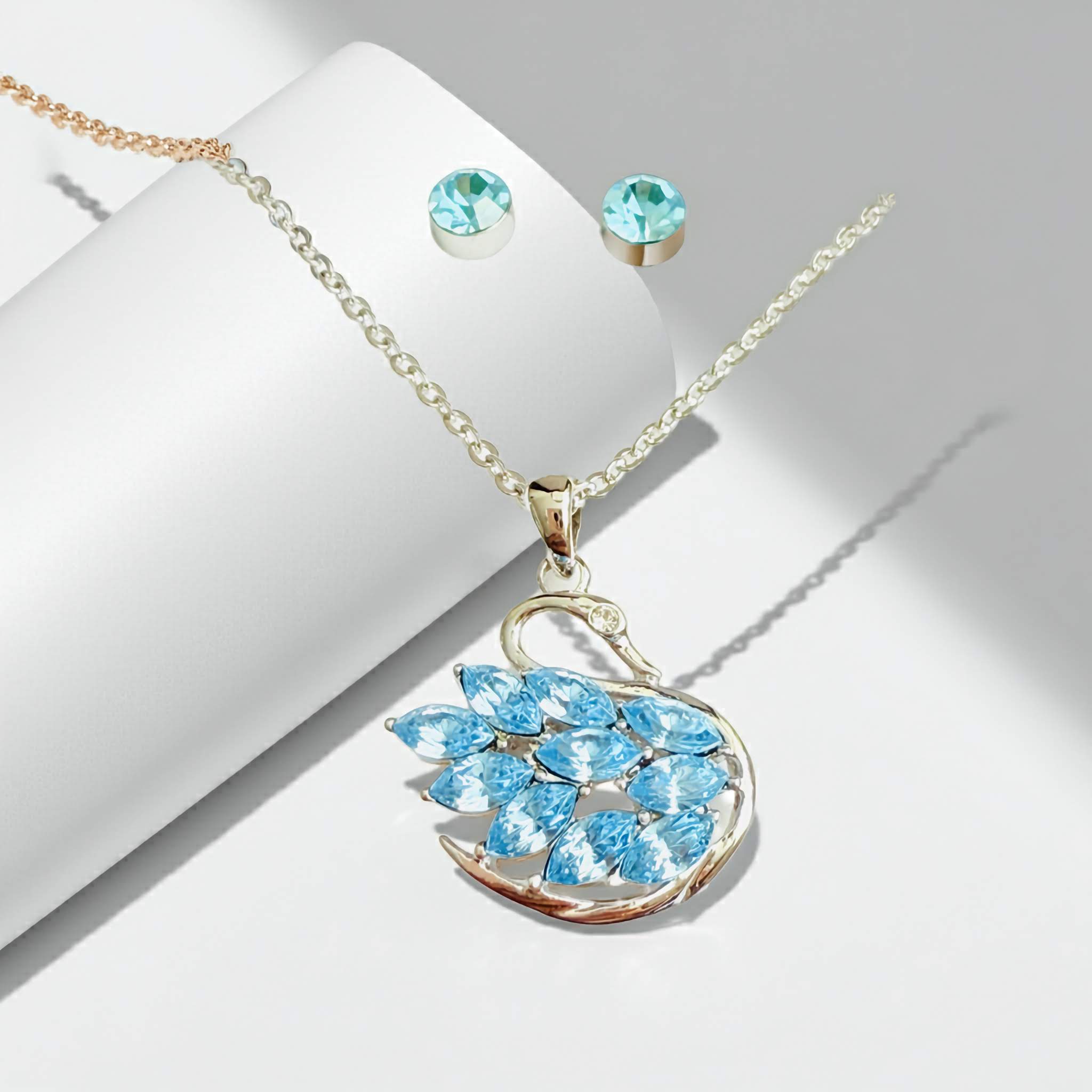 A Swarovski Jewelry set with blue gemstone Swan pendant and earrings on a white surface