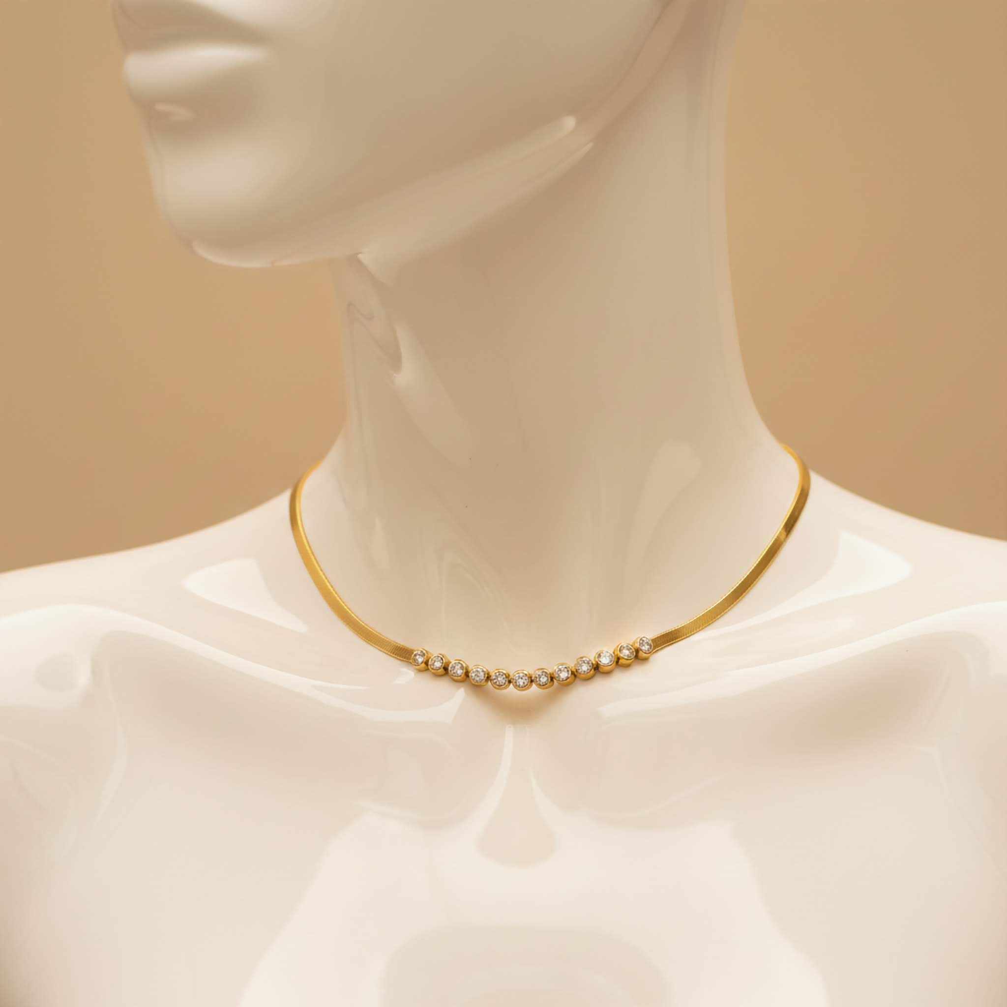 Mannequin wearing a gold necklace of clear gemstones against a beige background