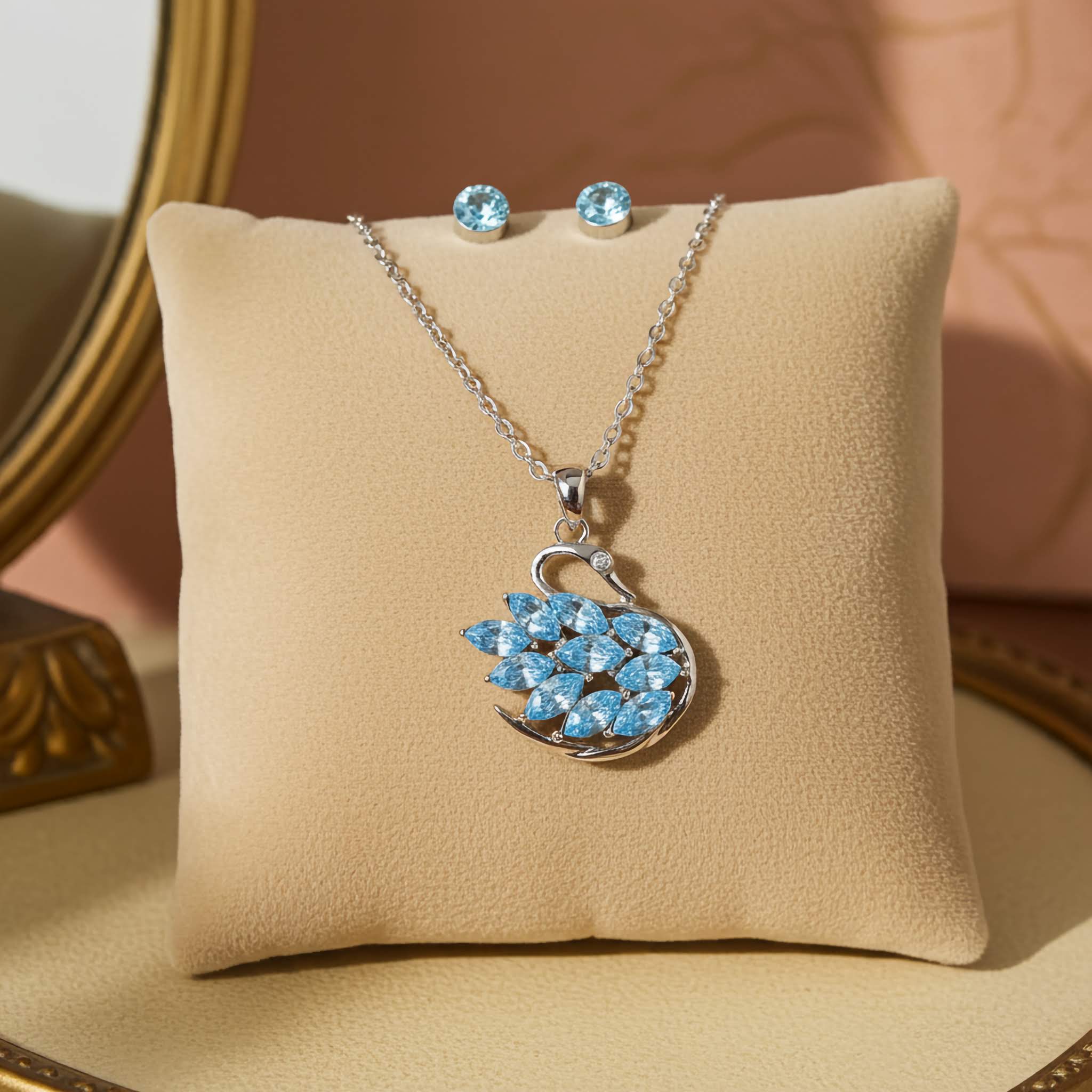 A Swarovski Swan Jewelry set with blue gemstone pendant and earrings on a beige cushion