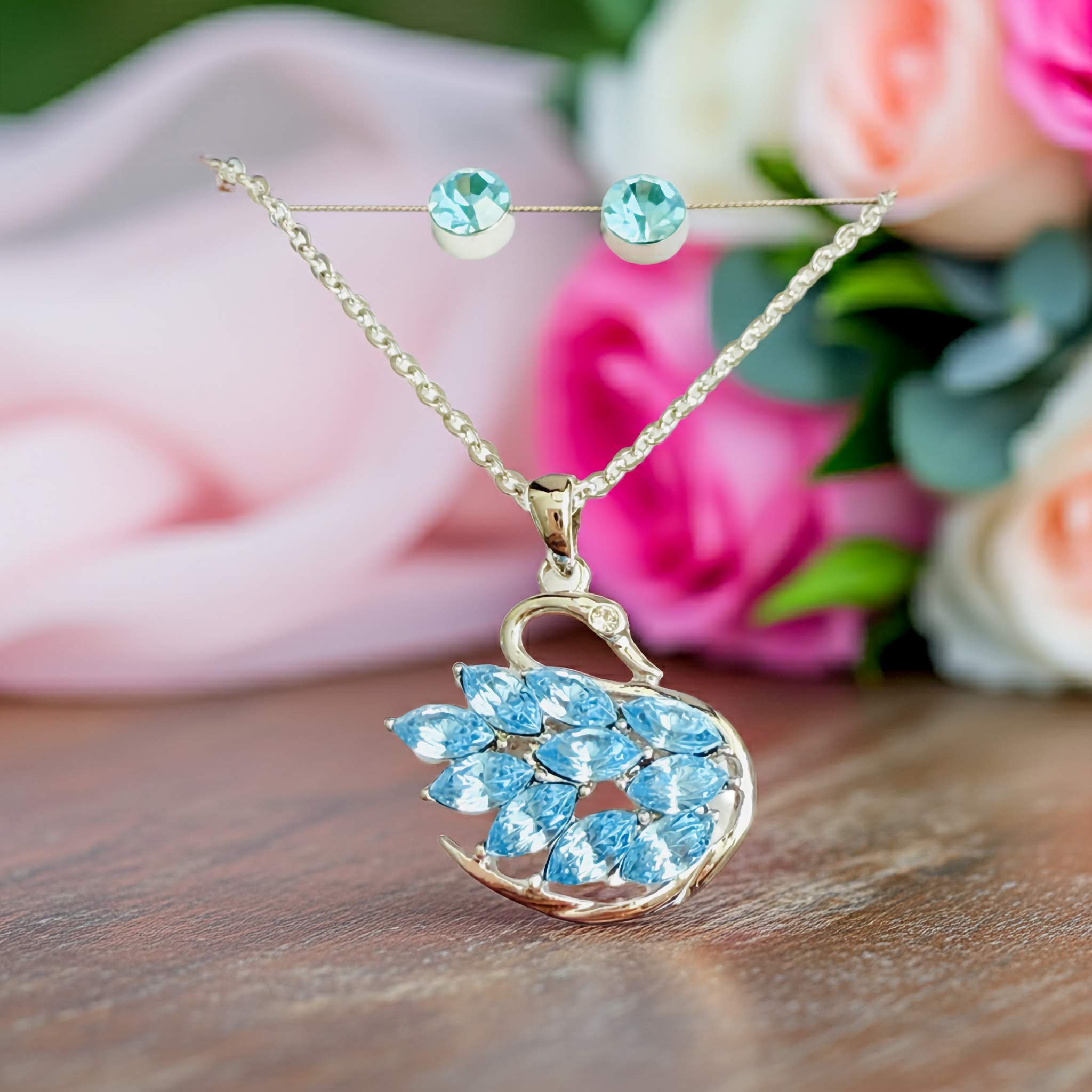 A silver Swarovski necklace with a swan pendant featuring blue stones against a floral background