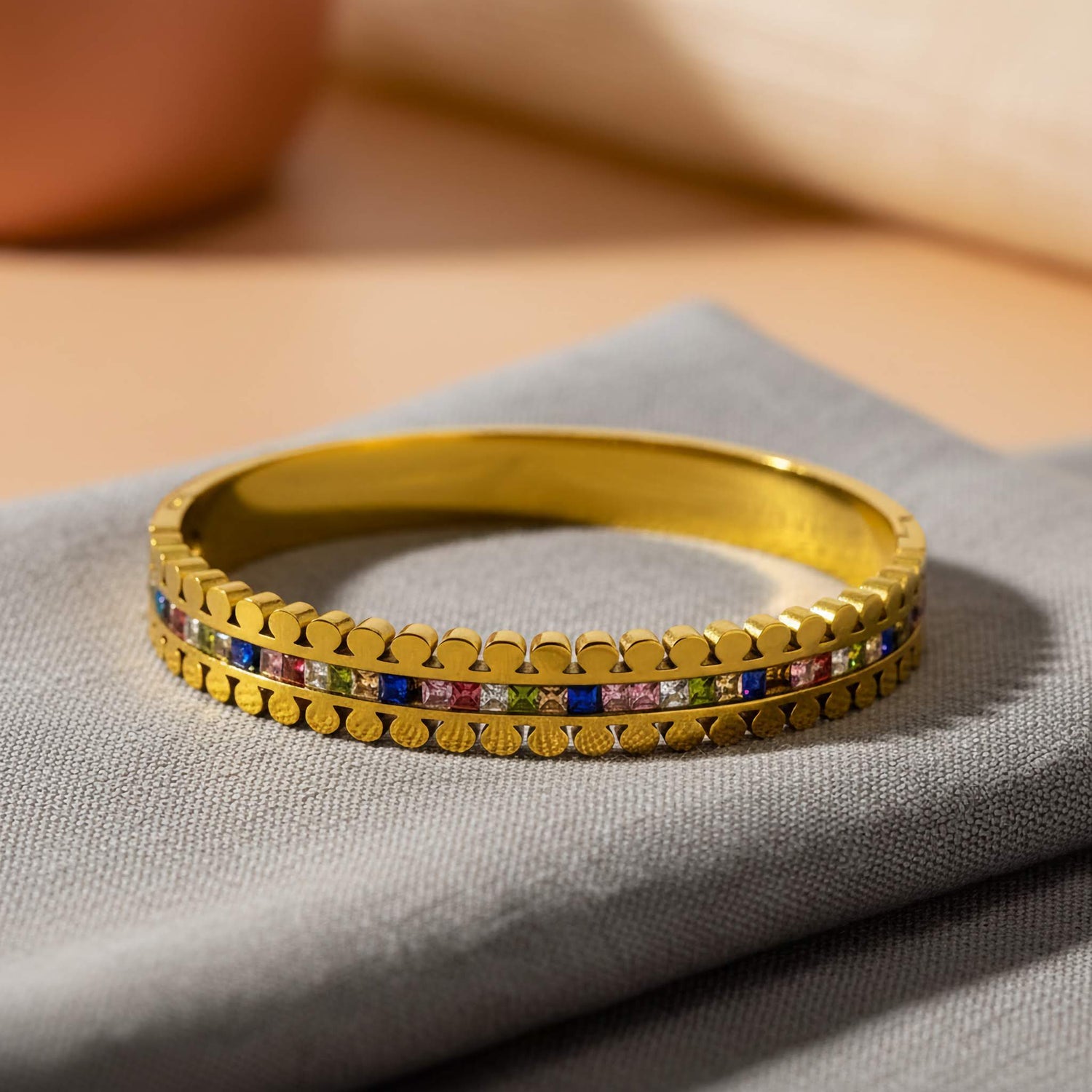 Buy imitation jewelry online - elegant gold bracelet with colorful accents on a soft fabric background.