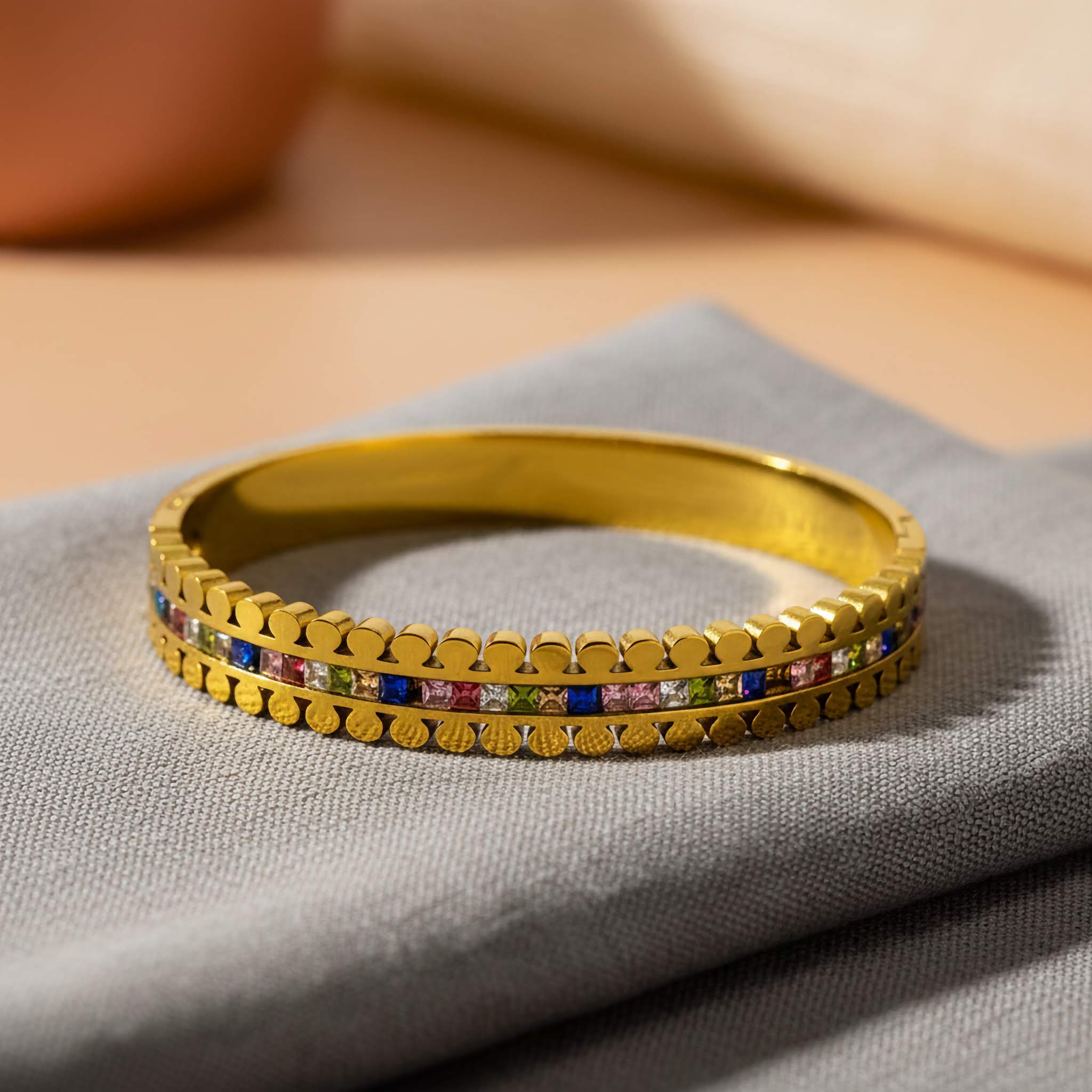 Buy imitation jewelry online - elegant gold bracelet with colorful accents on a soft fabric background.